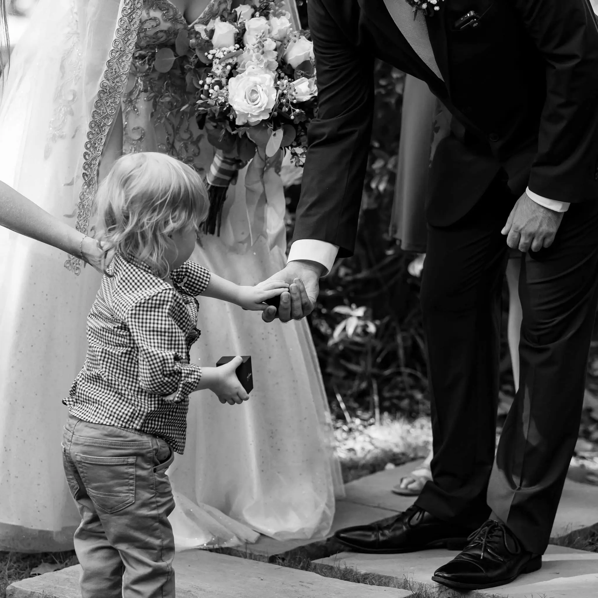 Little ring bearer reaching up to the groom with the ring box beside the bride