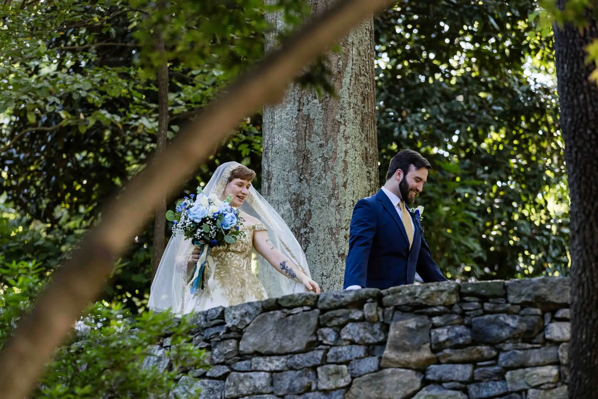 Couple walking along an old stone wall framed by tree branches in the garden