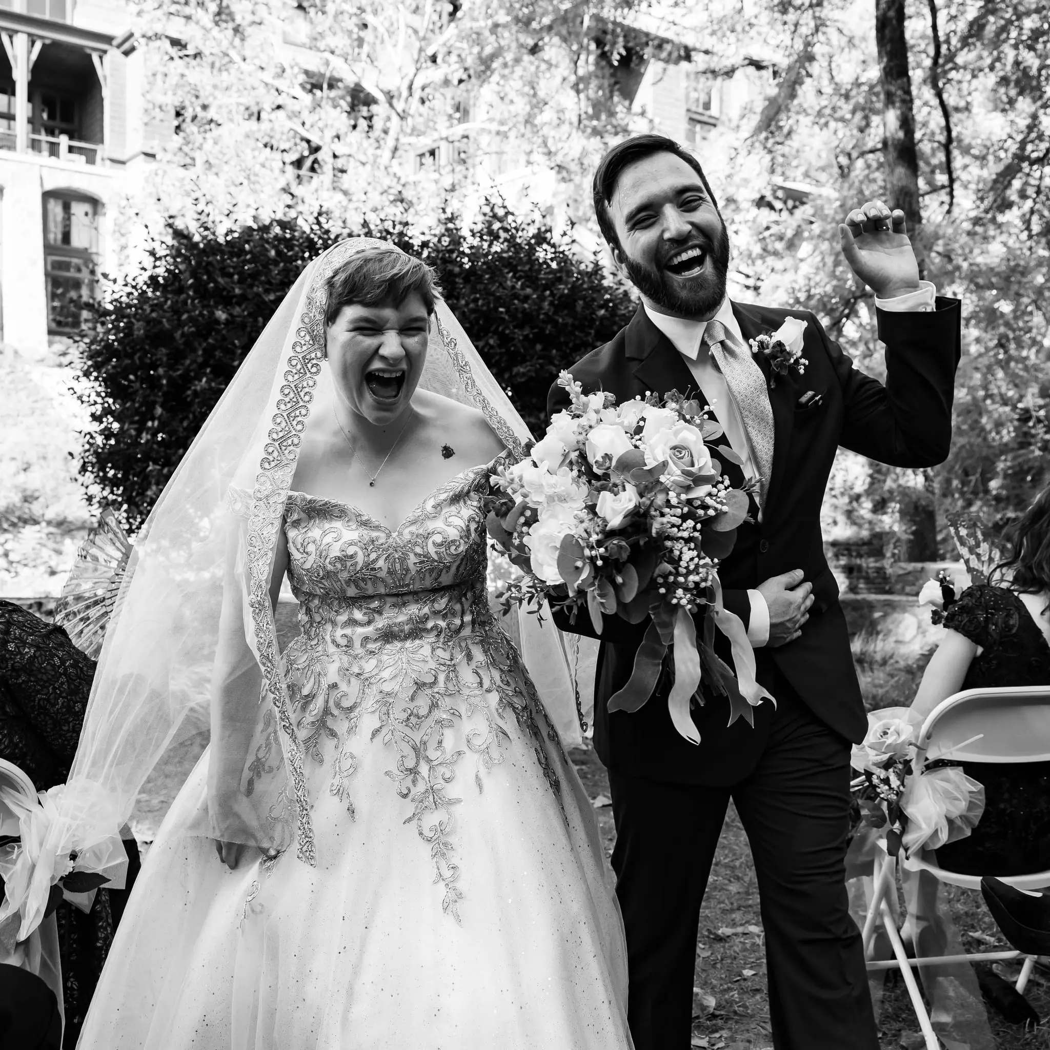 Black and white of Jessica and Hayden laughing with fists raised as they walk up the ceremony aisle
