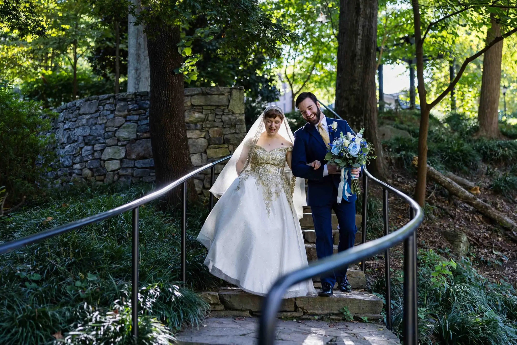 Jessica and Hayden wedding at Grand Bohemian Lodge Greenville, SC — the bride in a gold-embroidered gown and veil on a curved garden staircase, the groom standing below