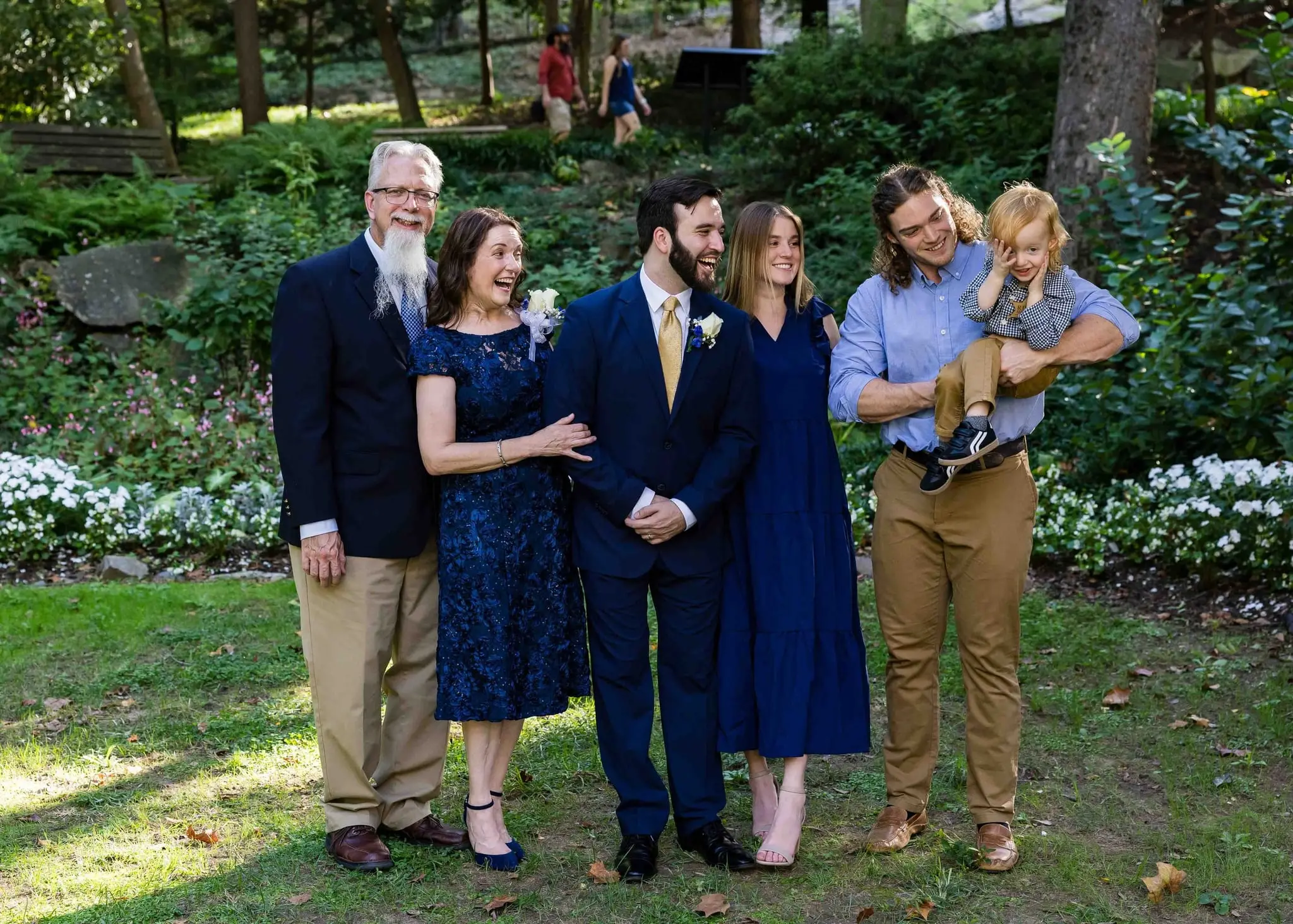Groom with family members, one holding a toddler, laughing together on the lawn