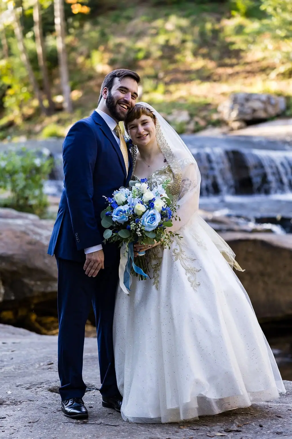 Hayden and Jessica hugging cheek to cheek on the rocks in front of a small waterfall