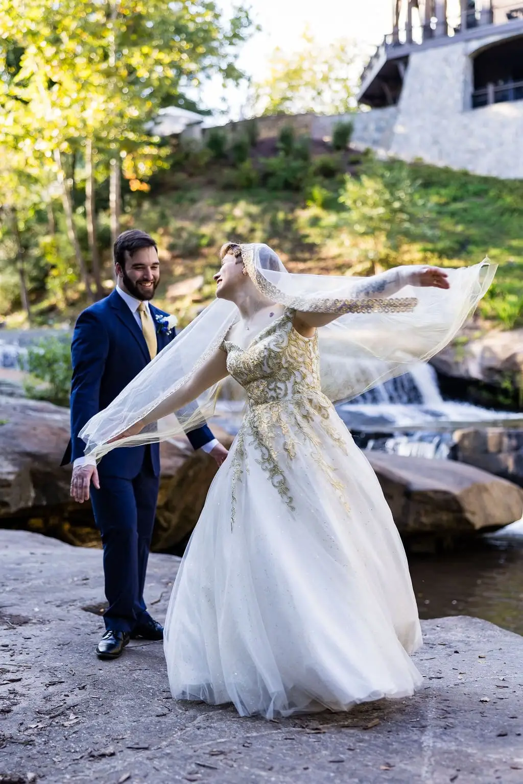 Jessica and Hayden wedding at Grand Bohemian Lodge Greenville, SC — the bride twirling her gown on rocks beside a waterfall as the groom watches
