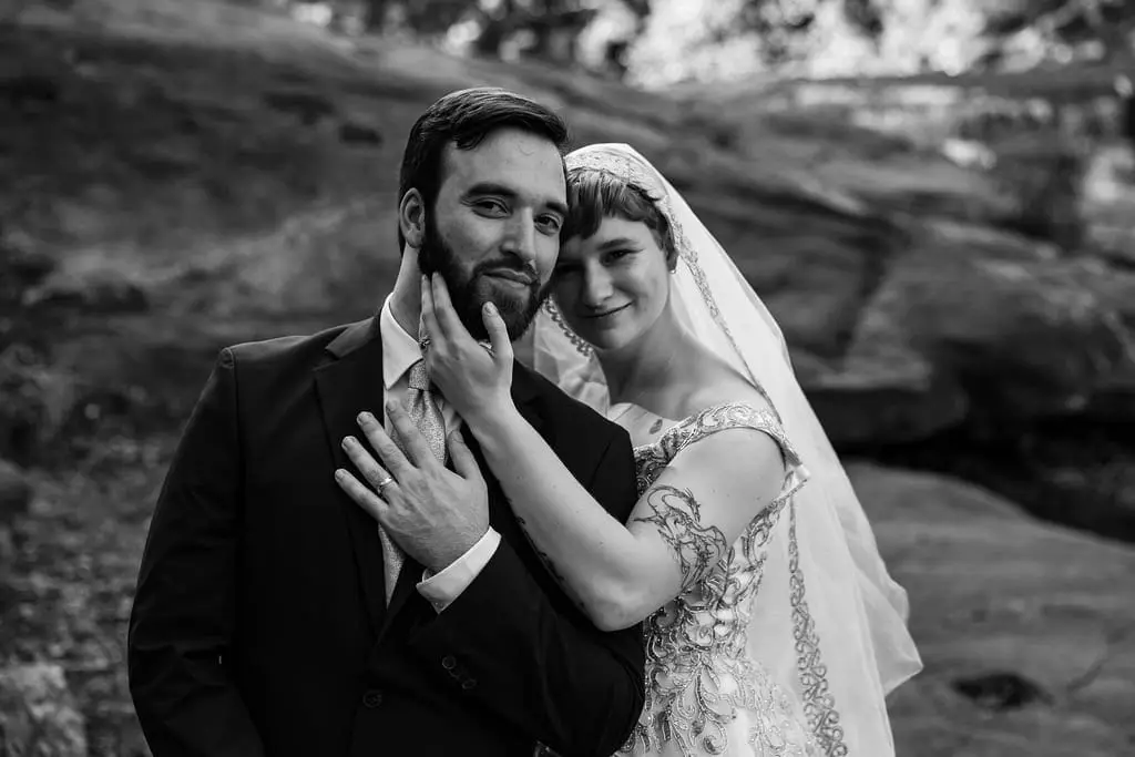 Black and white portrait of the groom with the bride's hand on his cheek and her head on his shoulder