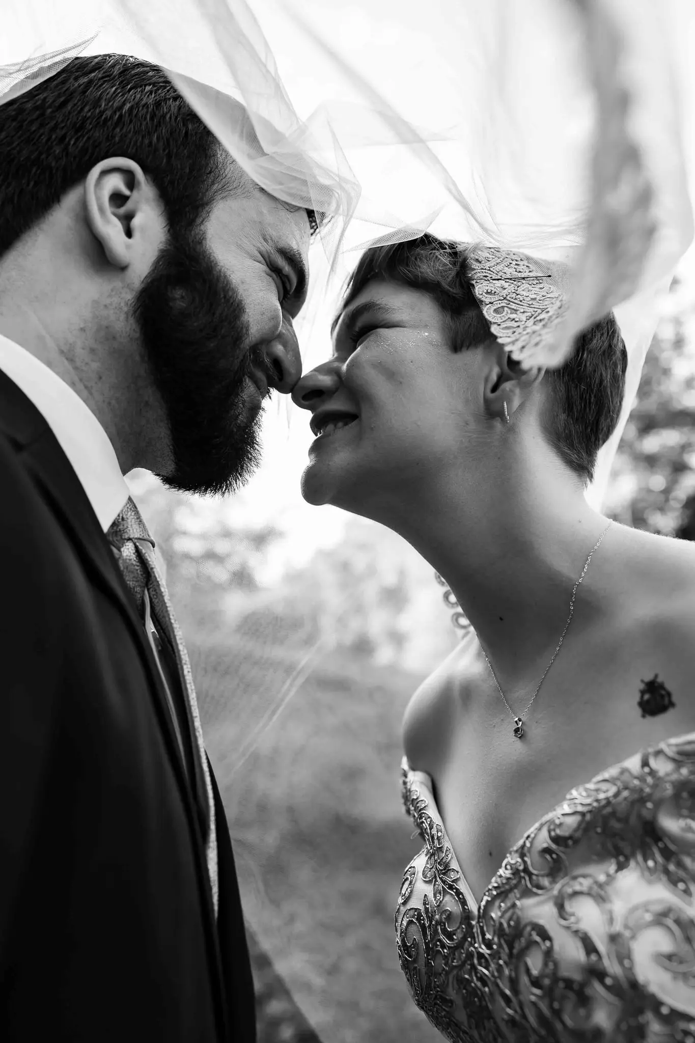 Black and white of the couple nose to nose beneath the veil