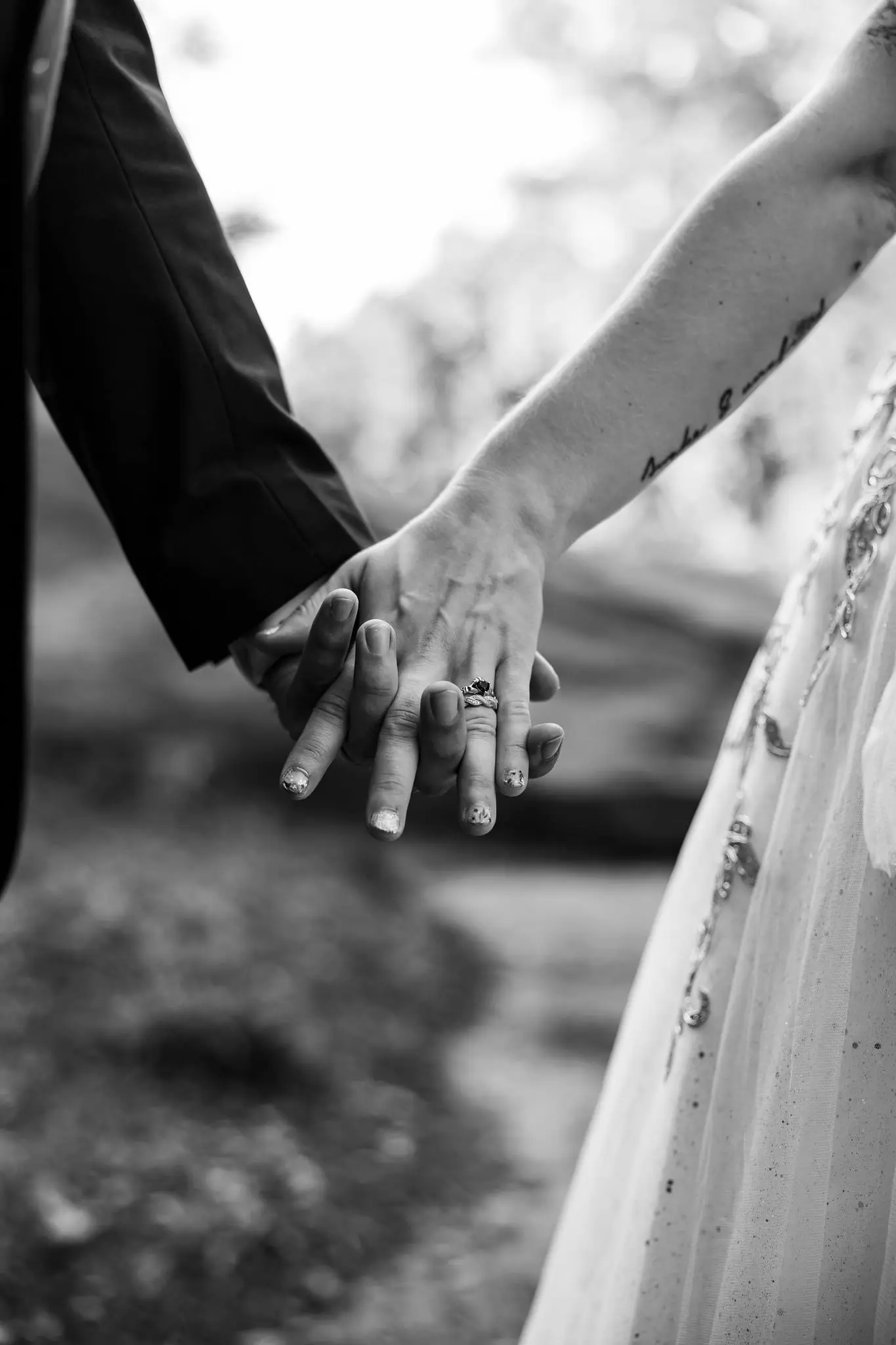 Black and white of the couple's joined hands with a wedding ring on the bride's finger