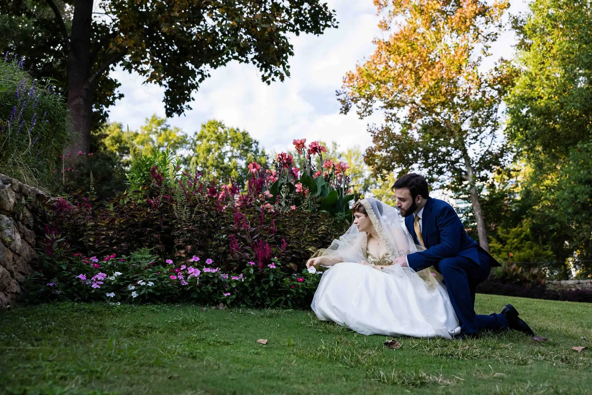 Jessica and Hayden wedding at Grand Bohemian Lodge Greenville, SC — the groom kneeling on the lawn in front of the bride among pink flowers
