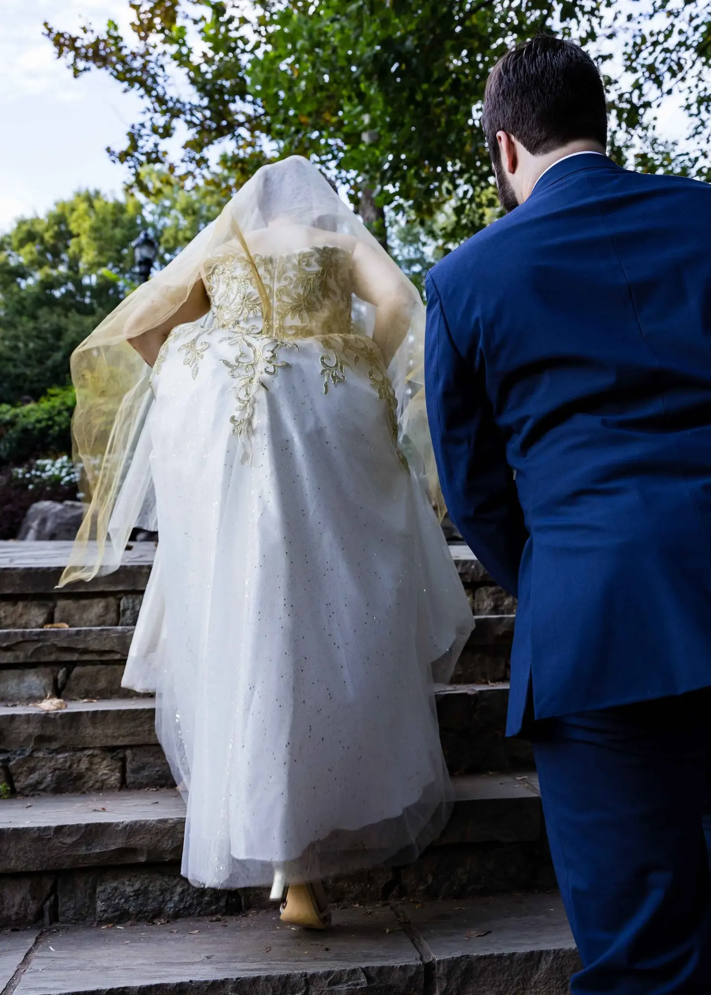 Bride in her veil climbing garden steps beside the groom in a navy suit