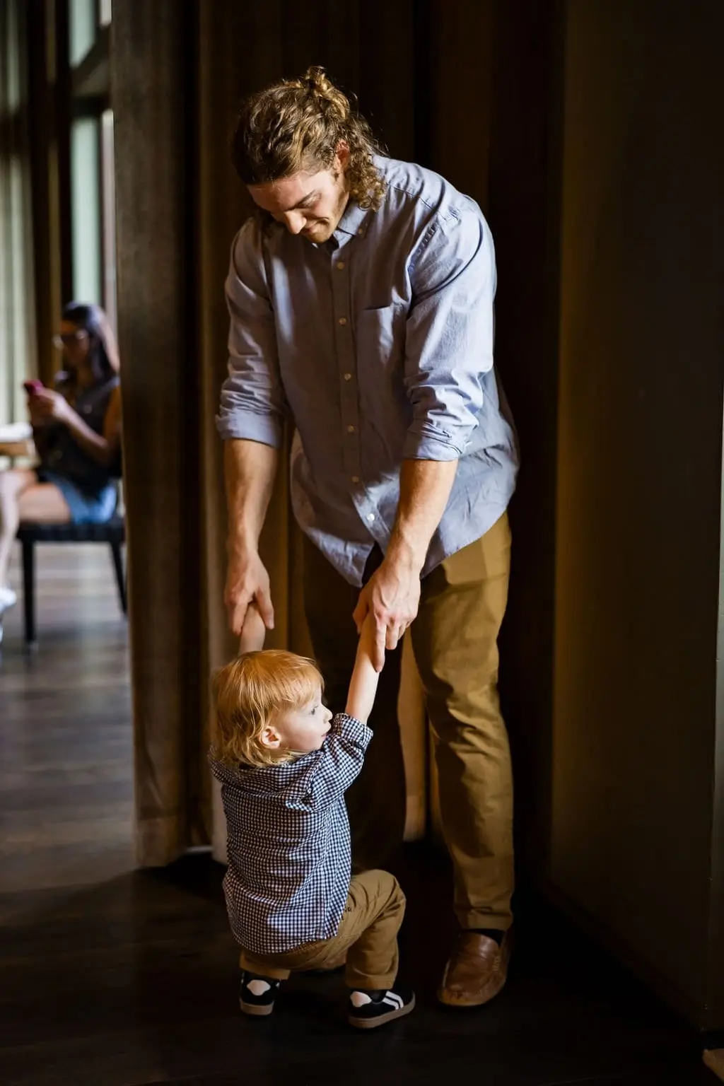 Man playfully swinging the toddler by his hands in a warm, dim hallway