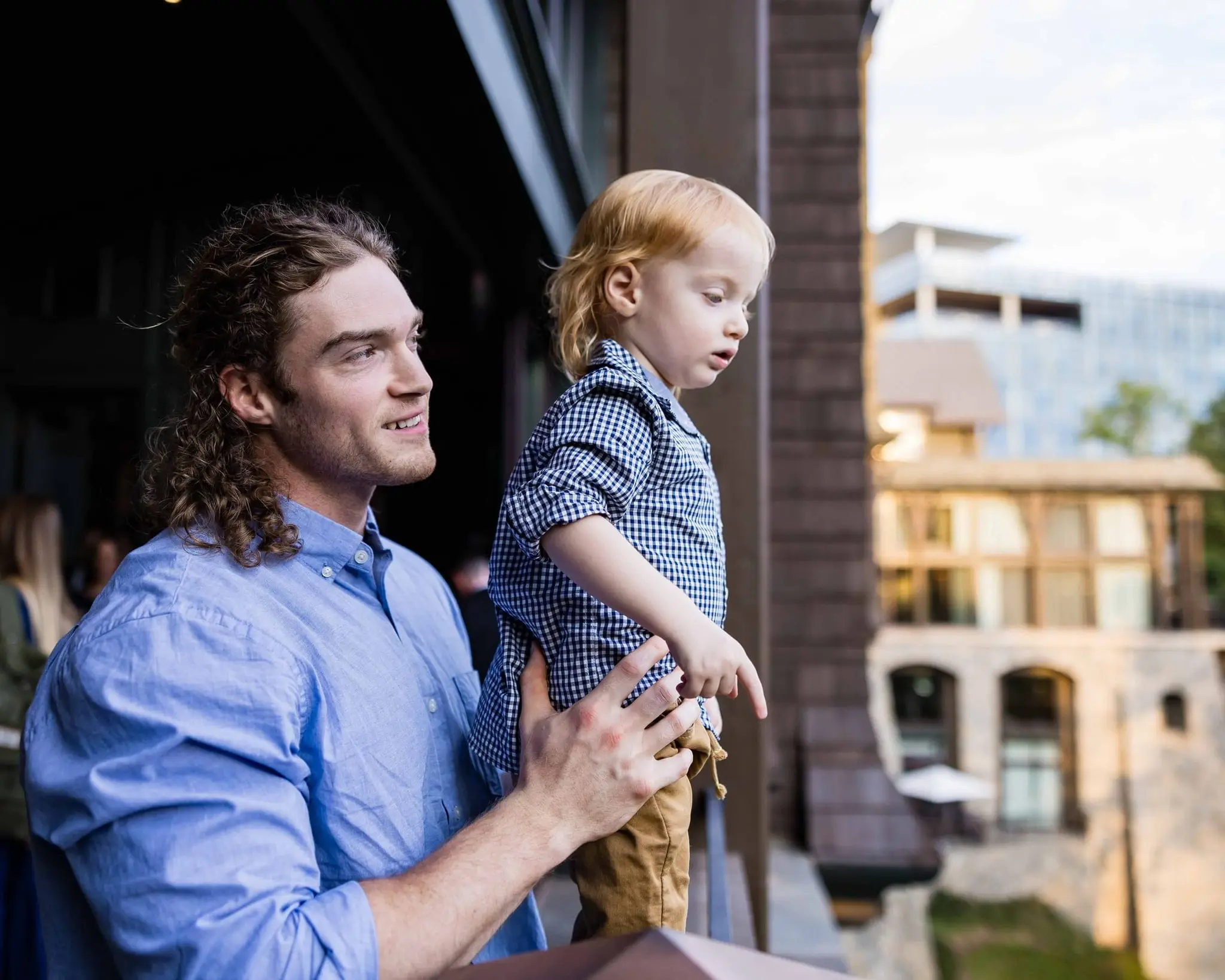 Man holding the toddler at a balcony railing, both looking out over the city and river