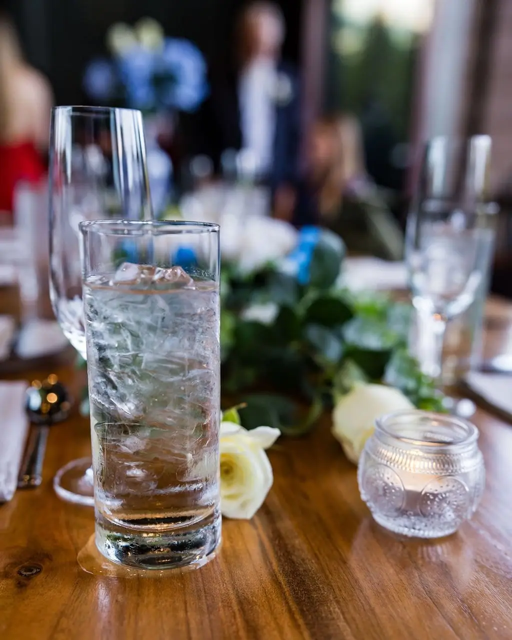 Iced water glass, candle and white roses on a wooden table set for the reception