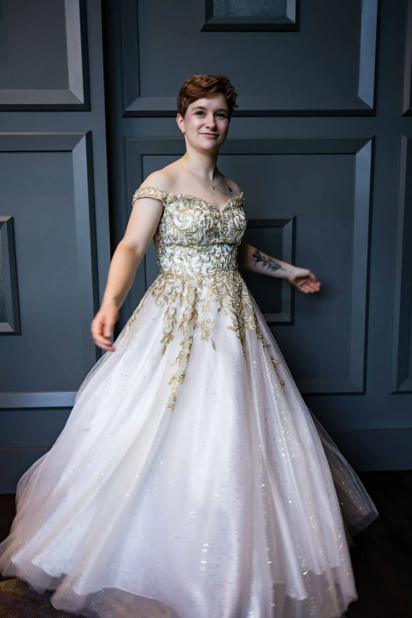 Jessica smiling and spinning in her gold-embroidered ball gown against a slate blue paneled wall