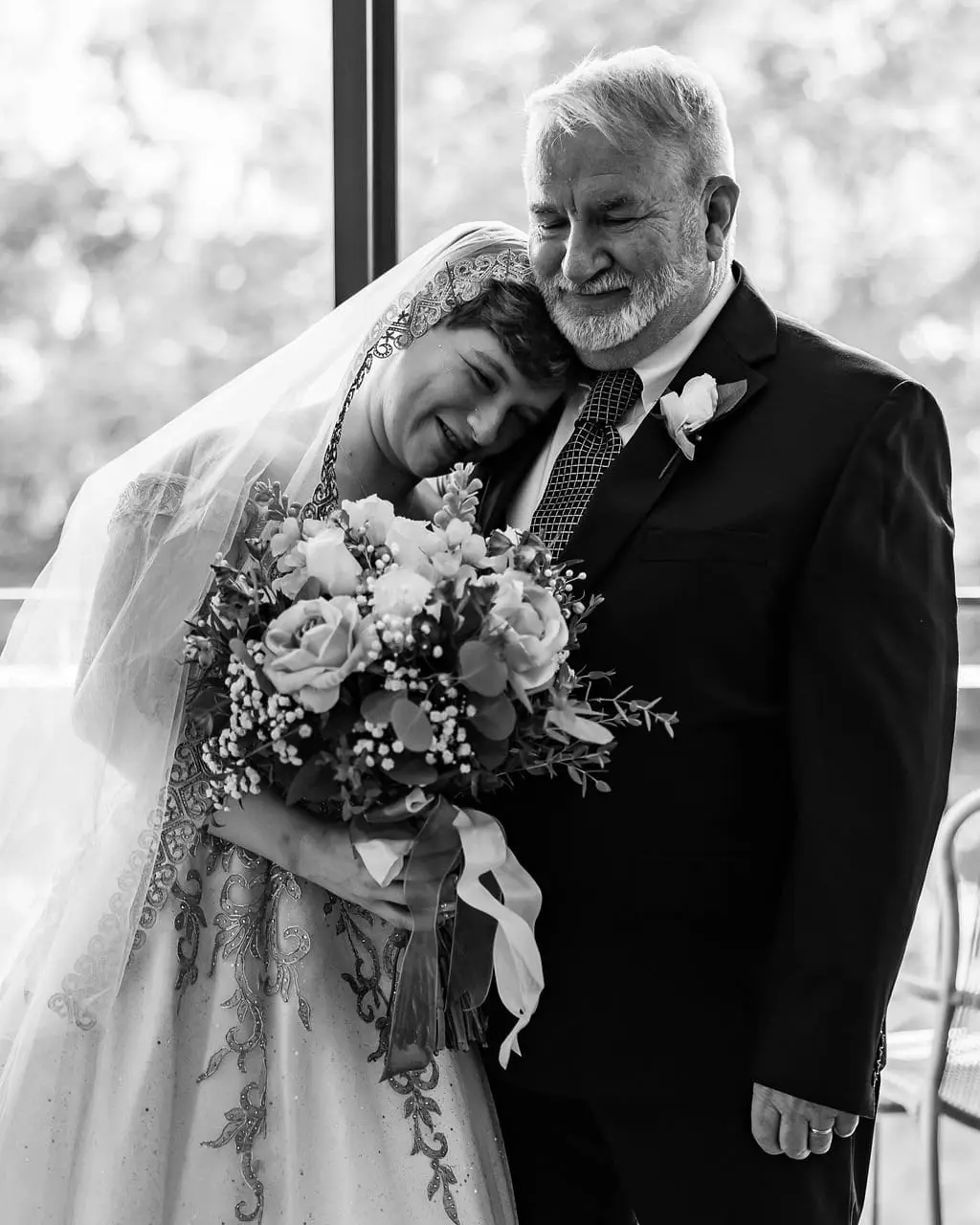 Jessica smiling as she rests her head against a gray-haired man in a dark suit, bouquet in hand, in black and white