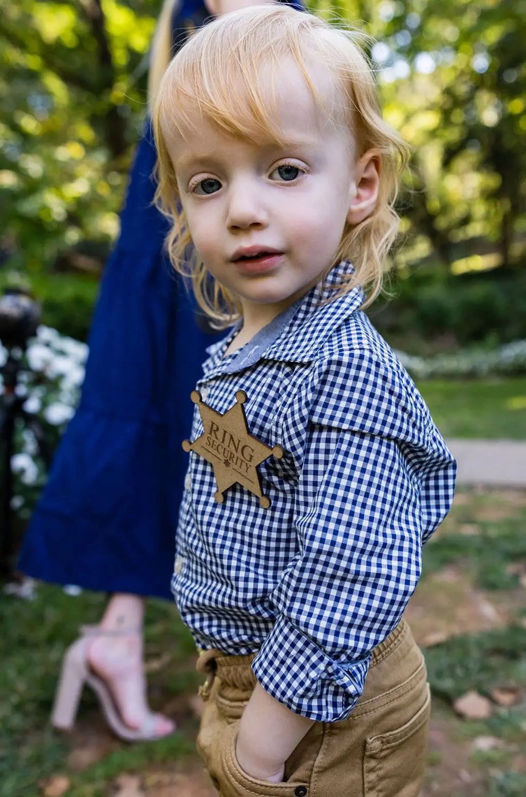 Toddler ring bearer in a gingham shirt wearing a wooden ring bearer badge