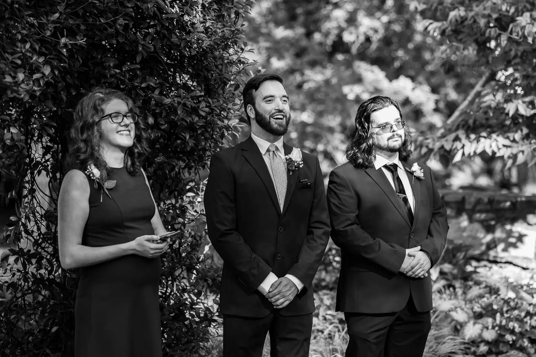 Black and white of the groomsmen and an attendant smiling as the ceremony begins