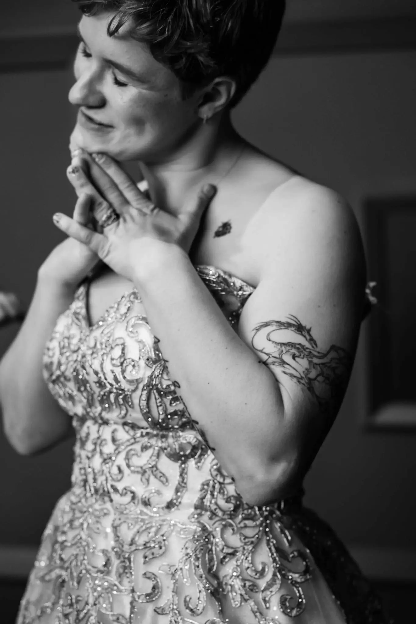 Black and white portrait of the bride clasping her hands to her chest, her beaded bodice and dragon tattoo visible