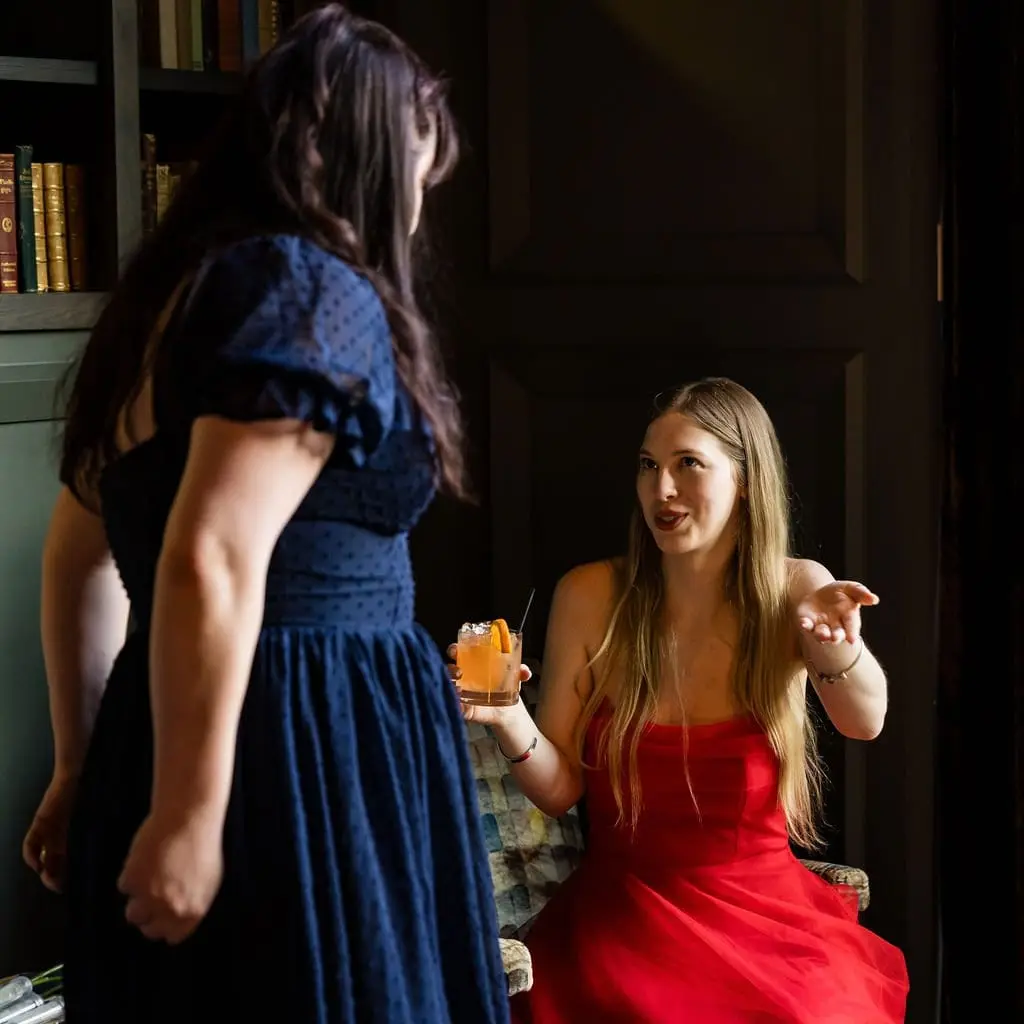 Two guests chatting, one in a red dress holding a cocktail, in the dim reception lounge