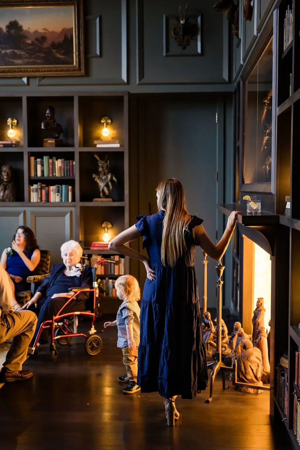 Guests relaxing in a warmly lit library lounge at the Grand Bohemian, a woman in blue by the fireplace