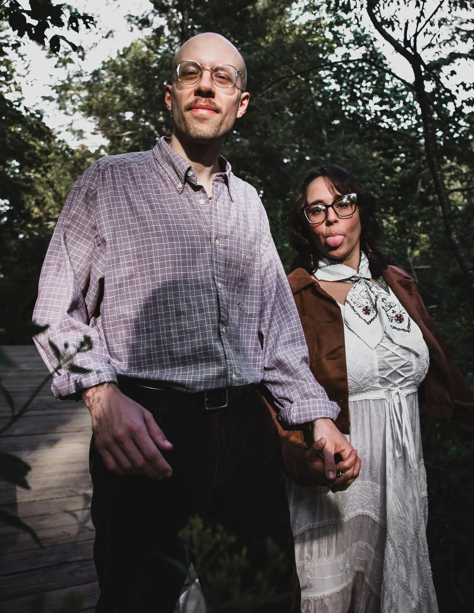 Couple holding hands in the woods, the woman playfully sticking out her tongue
