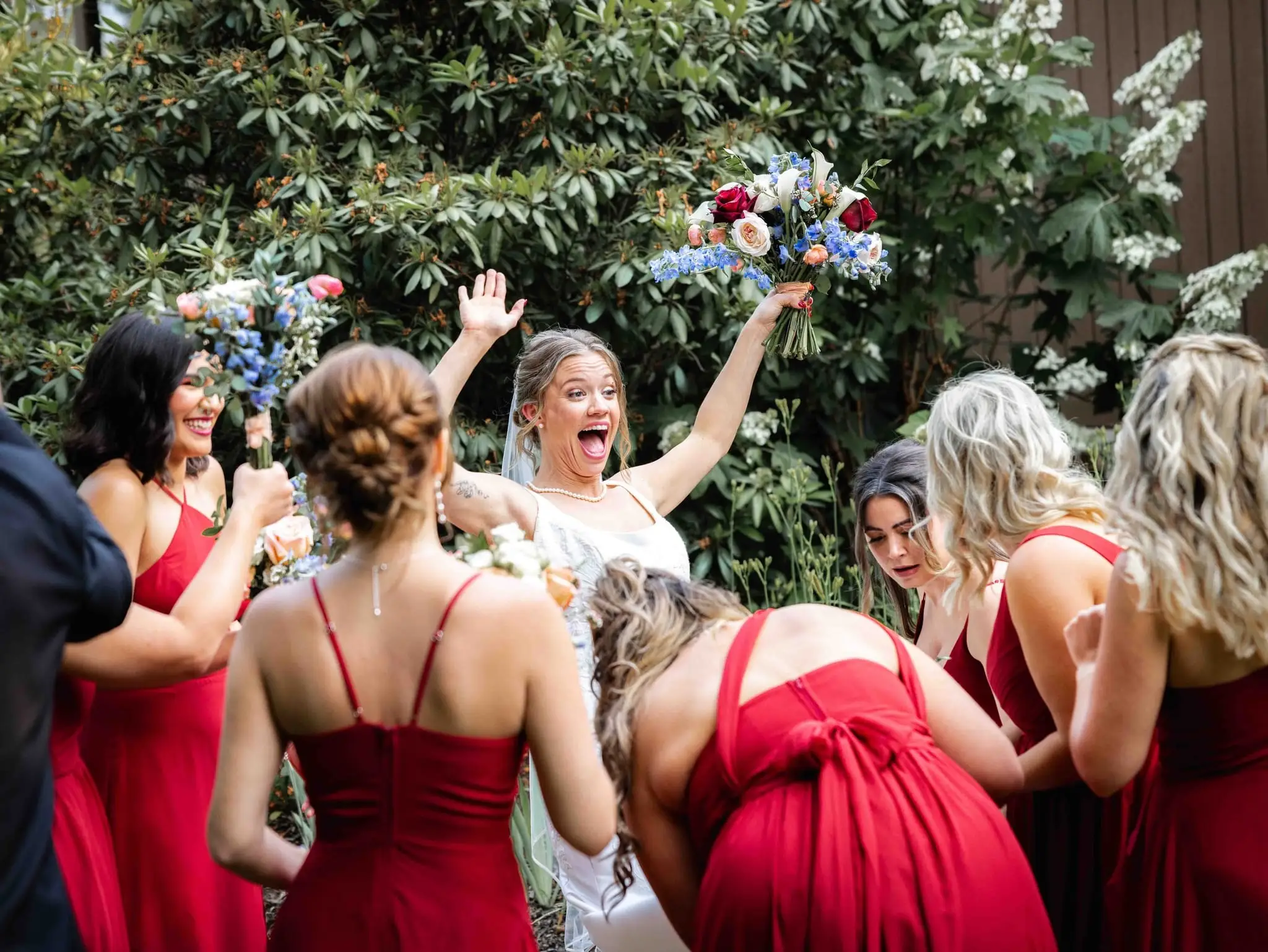 Anna and Joseph wedding at The Crest Center & Pavilion, Asheville NC — bridesmaids in red dresses cheering around the bride with bouquets raised