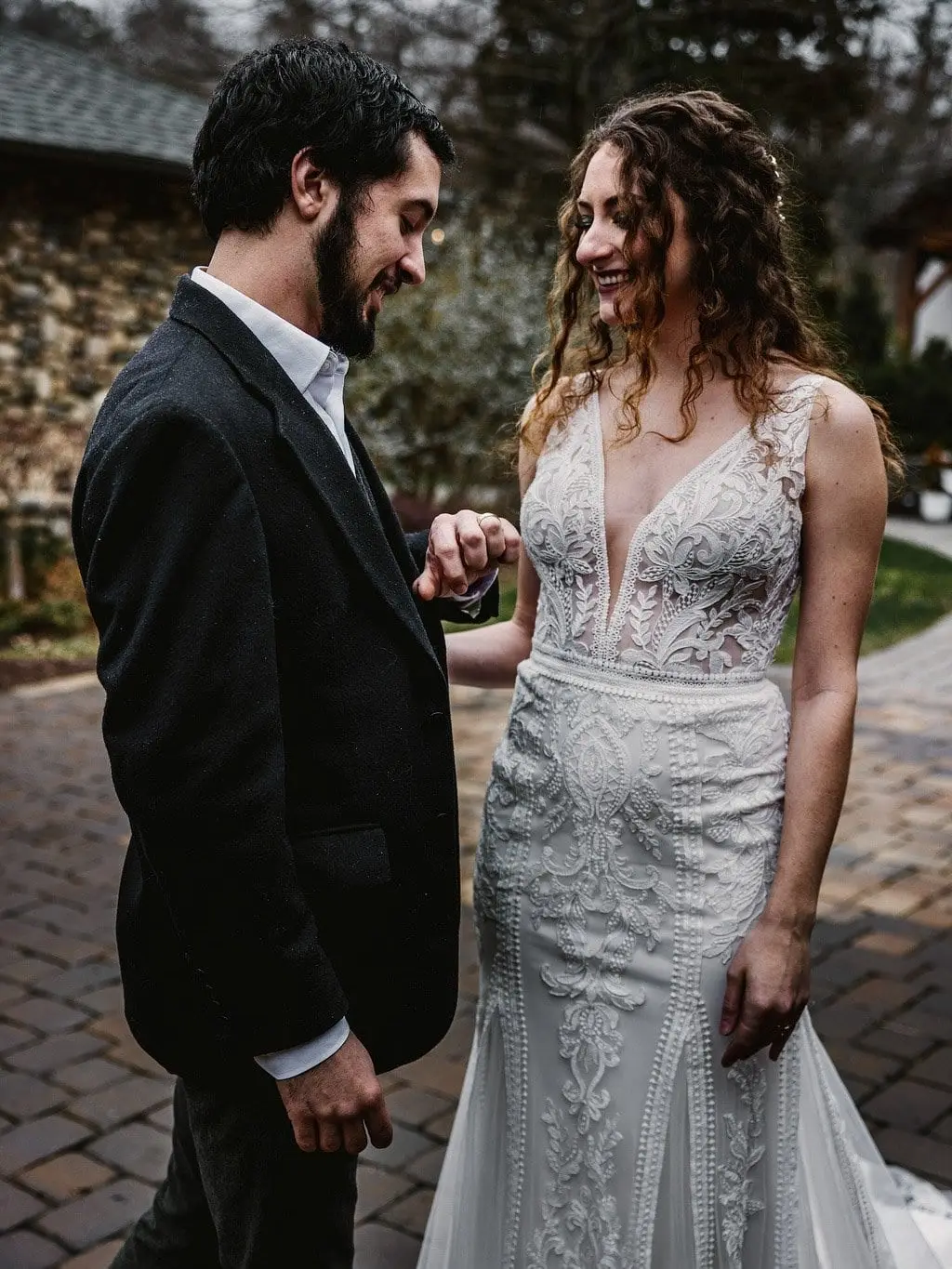 Bride laughs as the groom looks down at her hand on a brick courtyard path