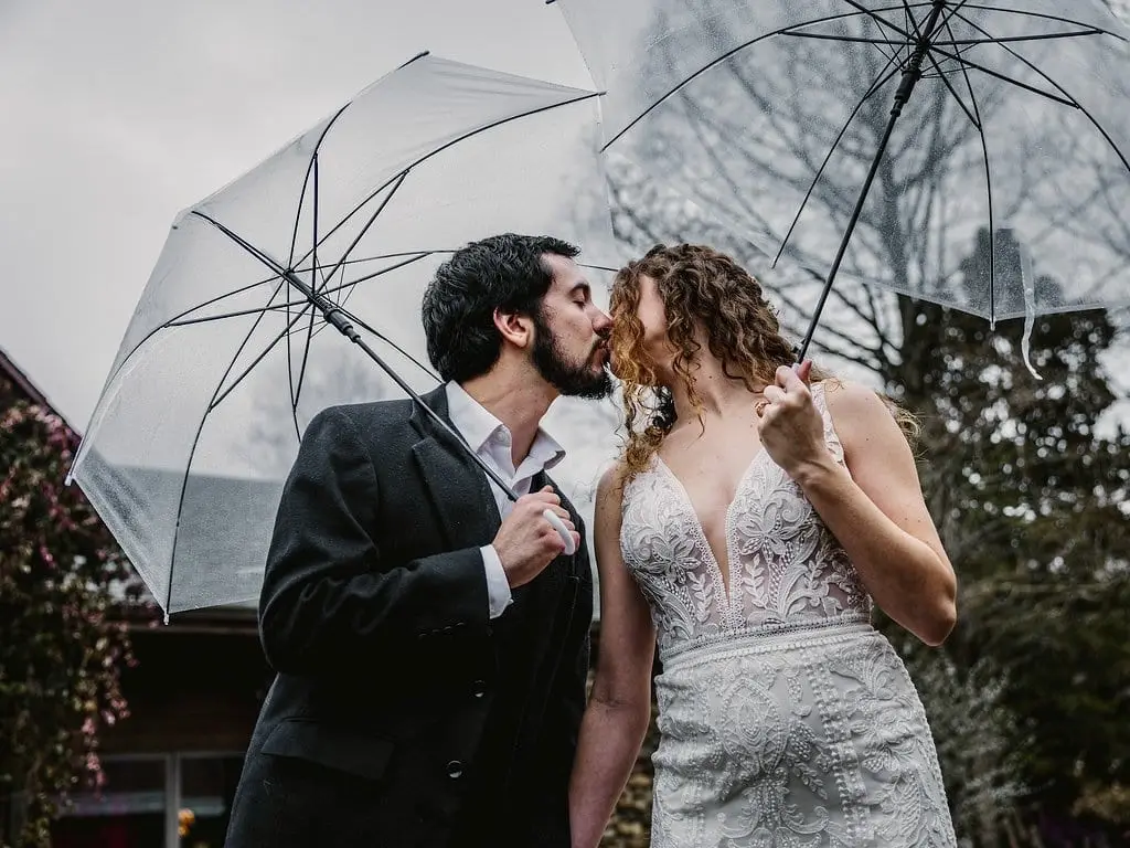 Couple share a kiss beneath clear umbrellas outside in the overcast Asheville weather