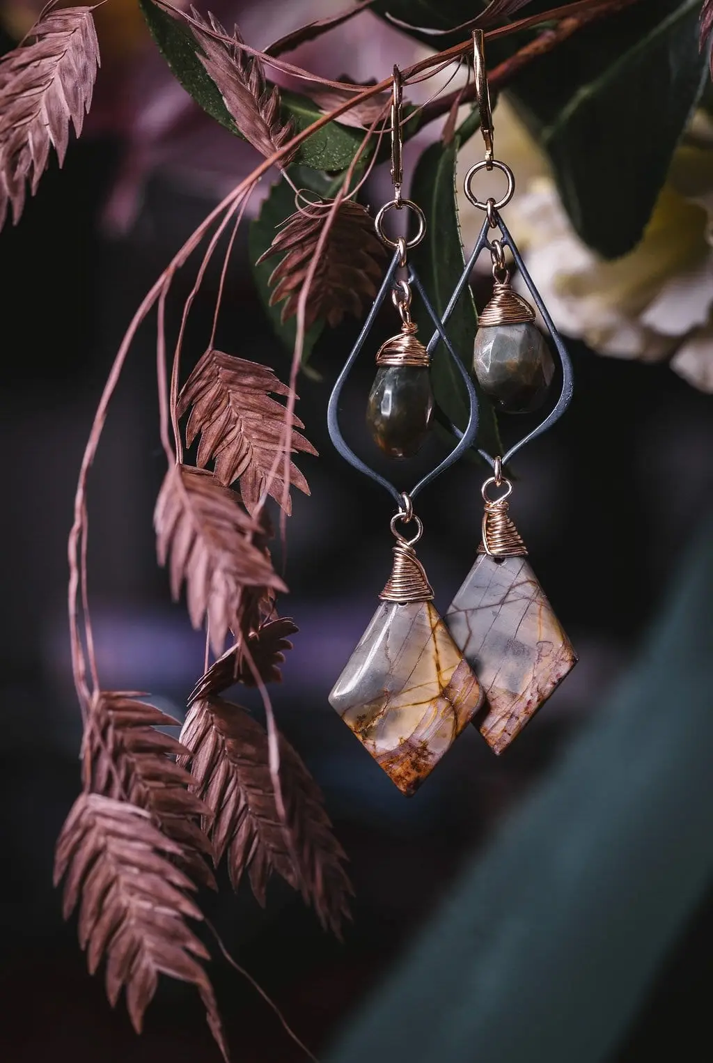 Wire-wrapped stone drop earrings hanging among dried pink grasses