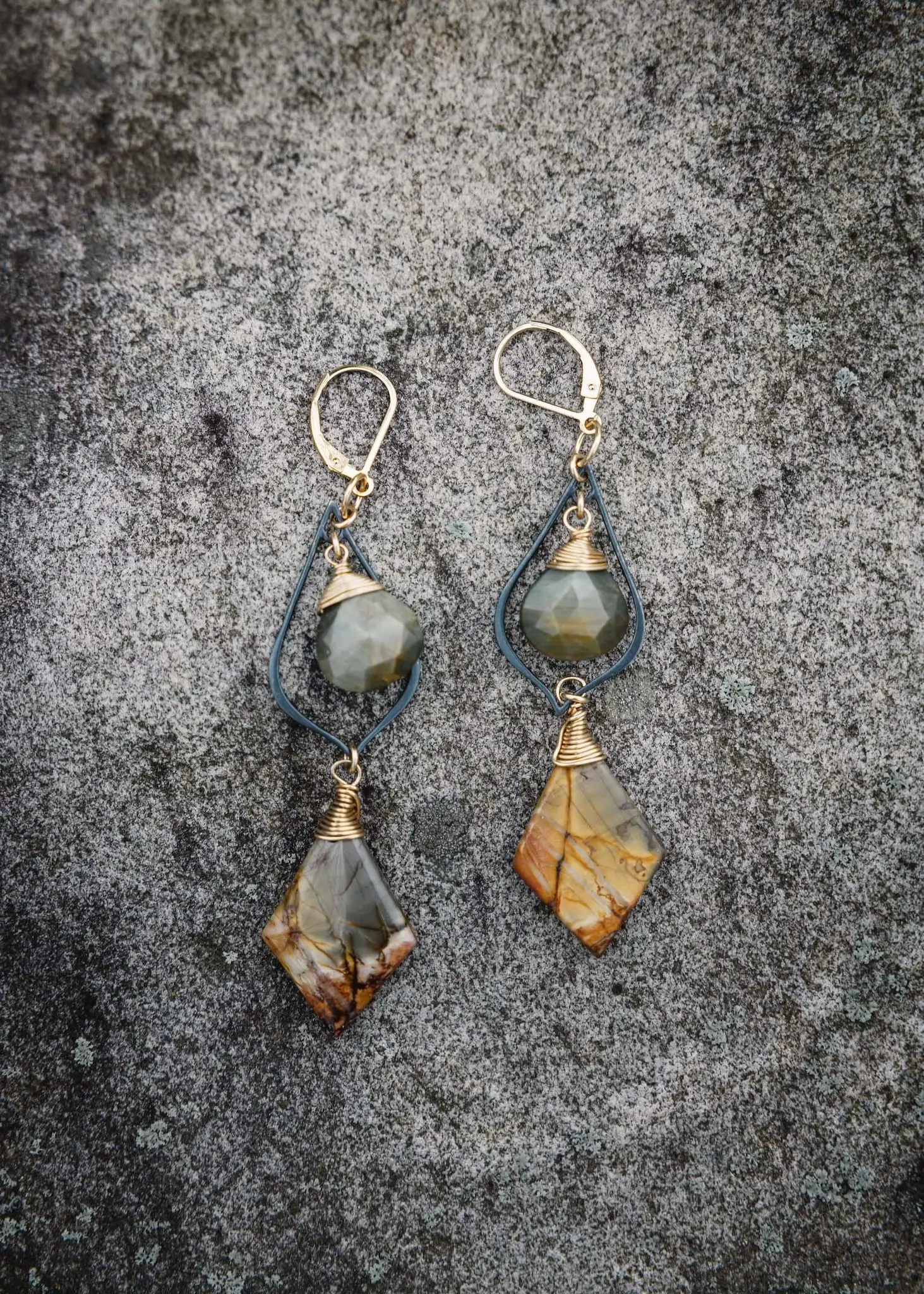 Pair of wire-wrapped stone earrings laid on gray granite