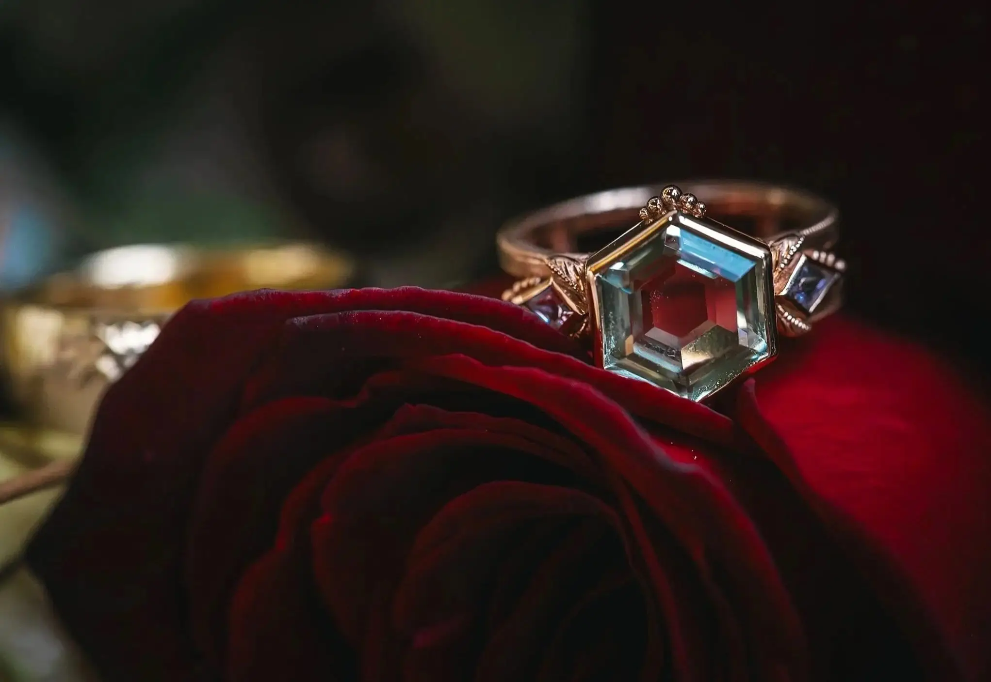 Hexagon-cut aquamarine ring resting on a dark red rose at a Haiku I Do styled shoot in Asheville