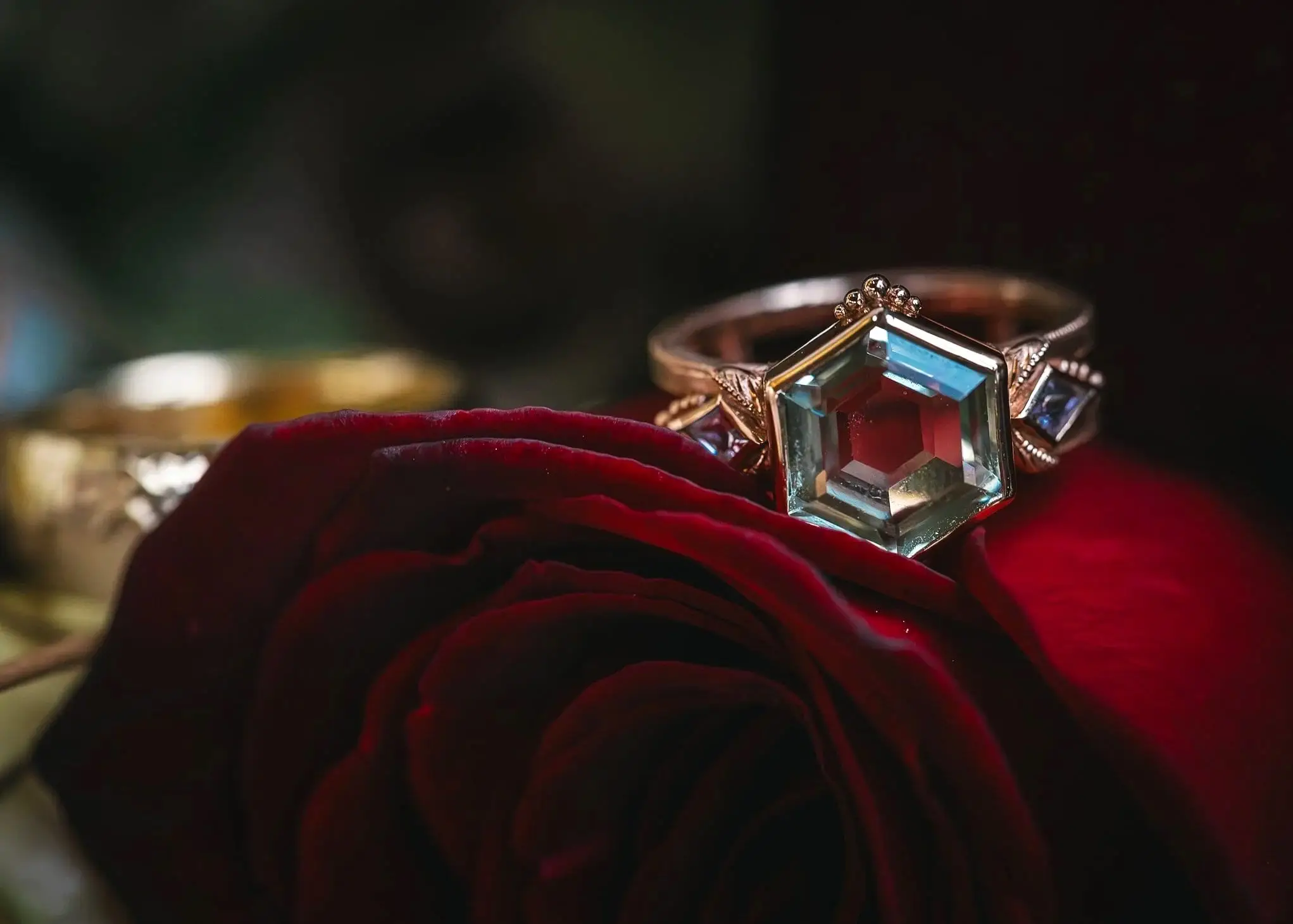 Hexagon-cut aquamarine ring resting on a dark red rose at a Haiku I Do styled shoot in Asheville