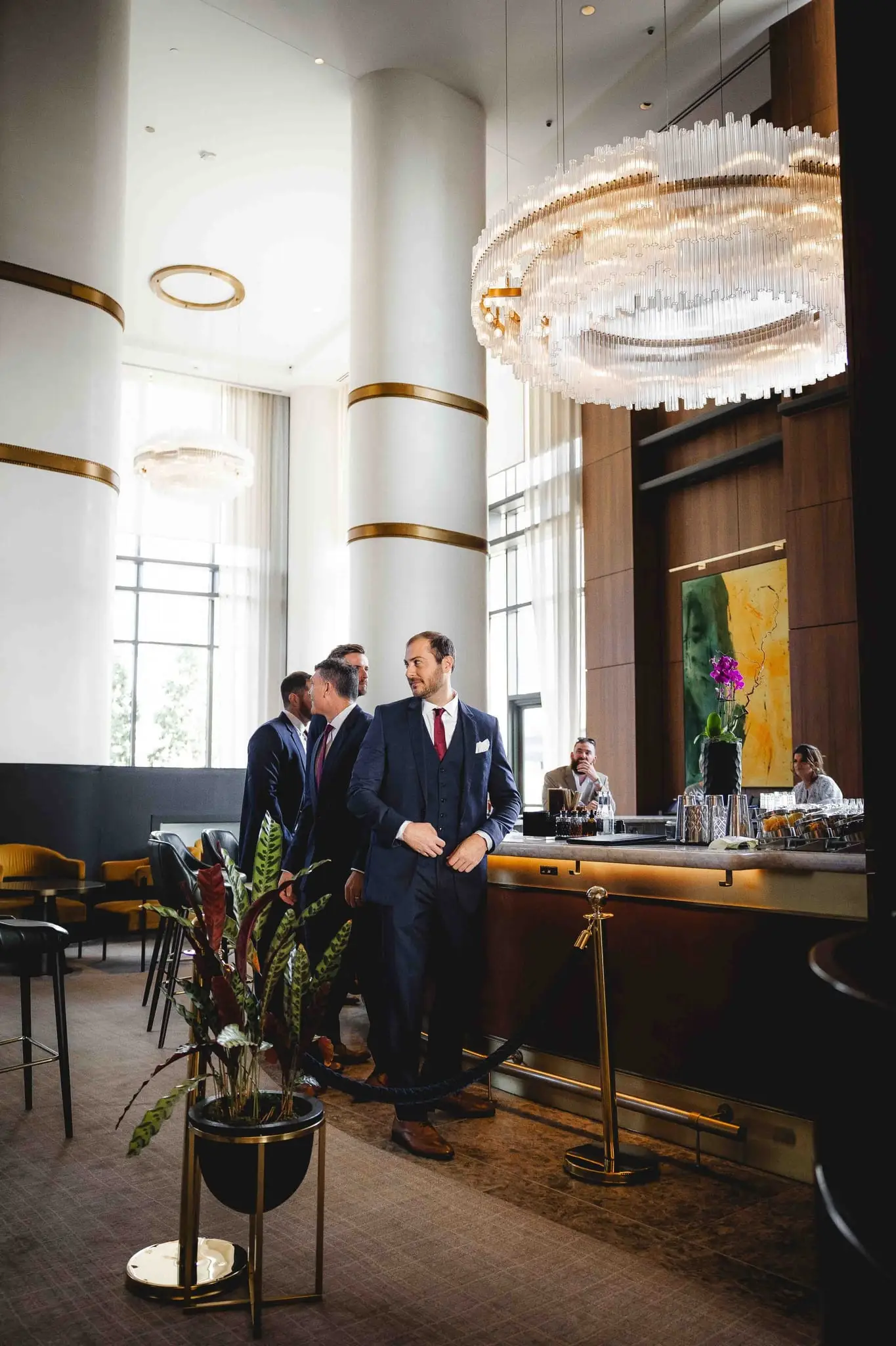 Ashley and Alex wedding at Conrad Nashville, Nashville TN — the groomsmen standing in a lounge under a large chandelier