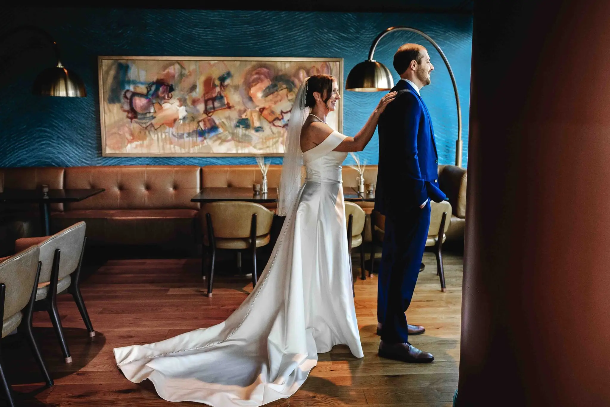 Ashley and Alex wedding at Conrad Nashville, Nashville TN — the couple in front of a teal wall with an abstract painting, her long train spread behind her