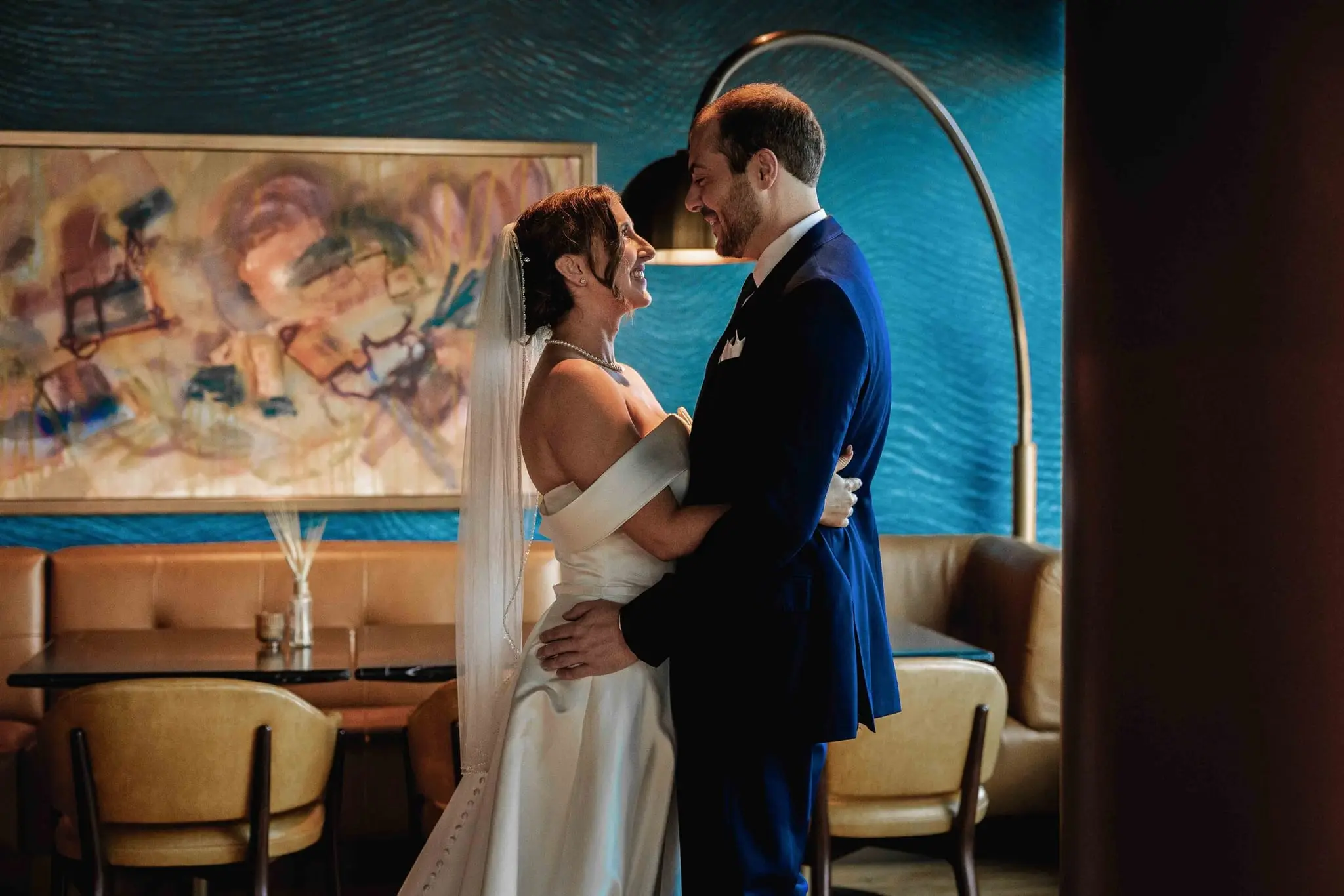 Couple embracing and smiling after the first look in front of a colorful abstract painting