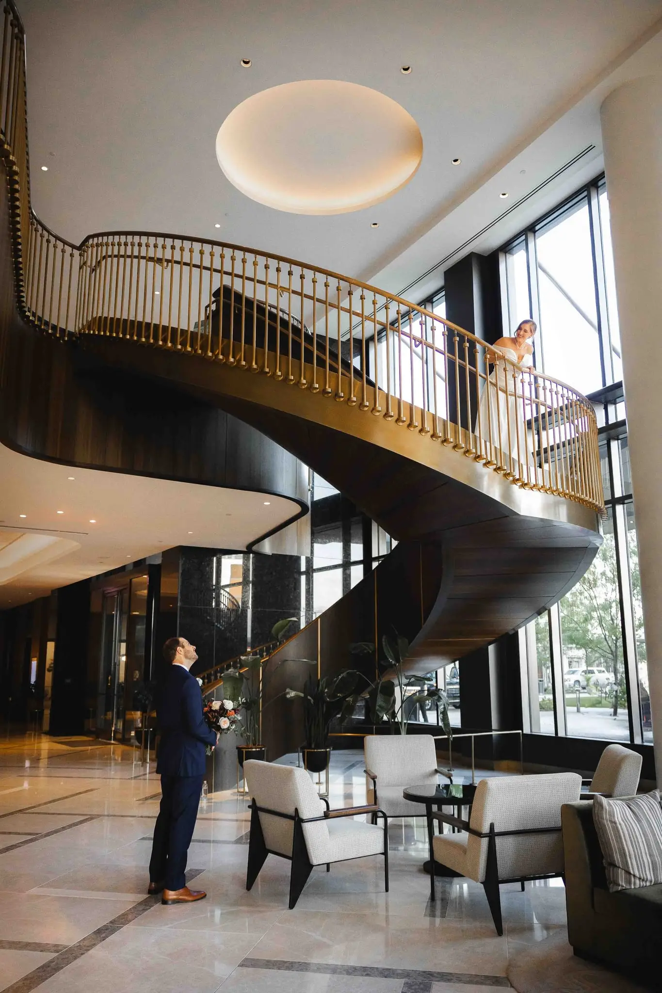 Ashley and Alex wedding at Conrad Nashville, Nashville TN — the groom waiting beneath a gold spiral staircase in the lobby