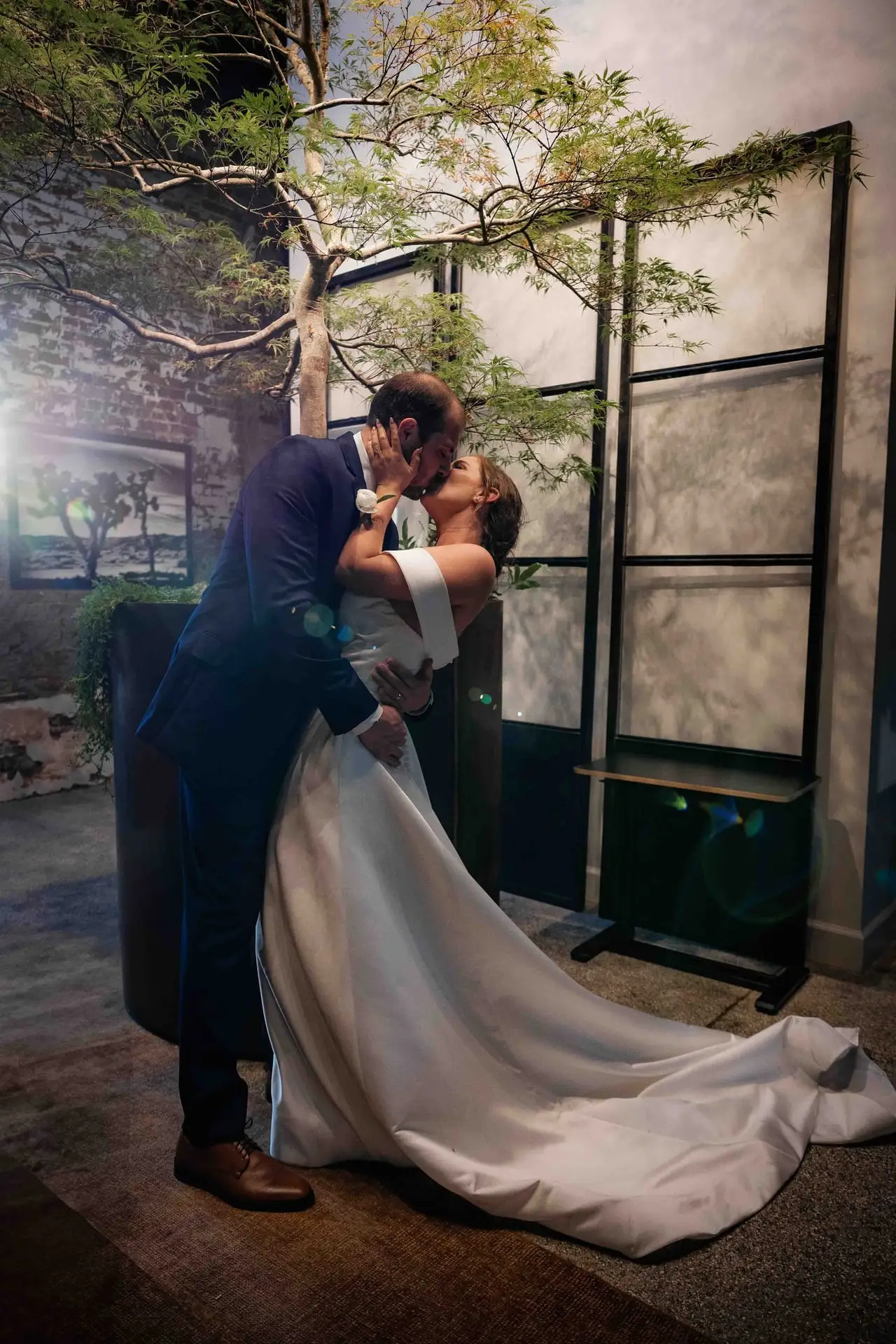 Ashley and Alex wedding at Conrad Nashville, Nashville TN — the groom dipping the bride in front of a tall glass door and a potted tree