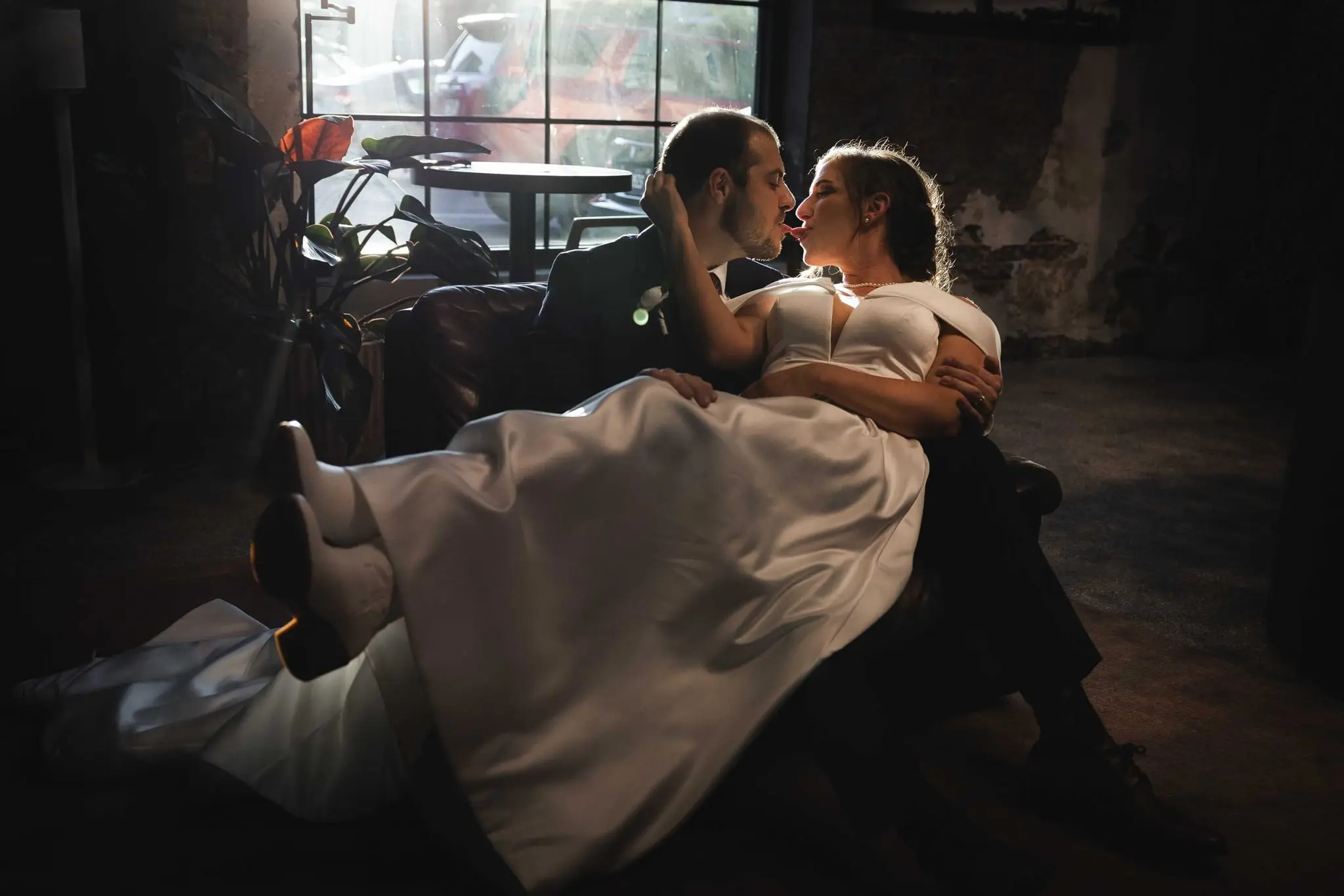 Wide view of the couple nestled together on a dark sofa by a large window