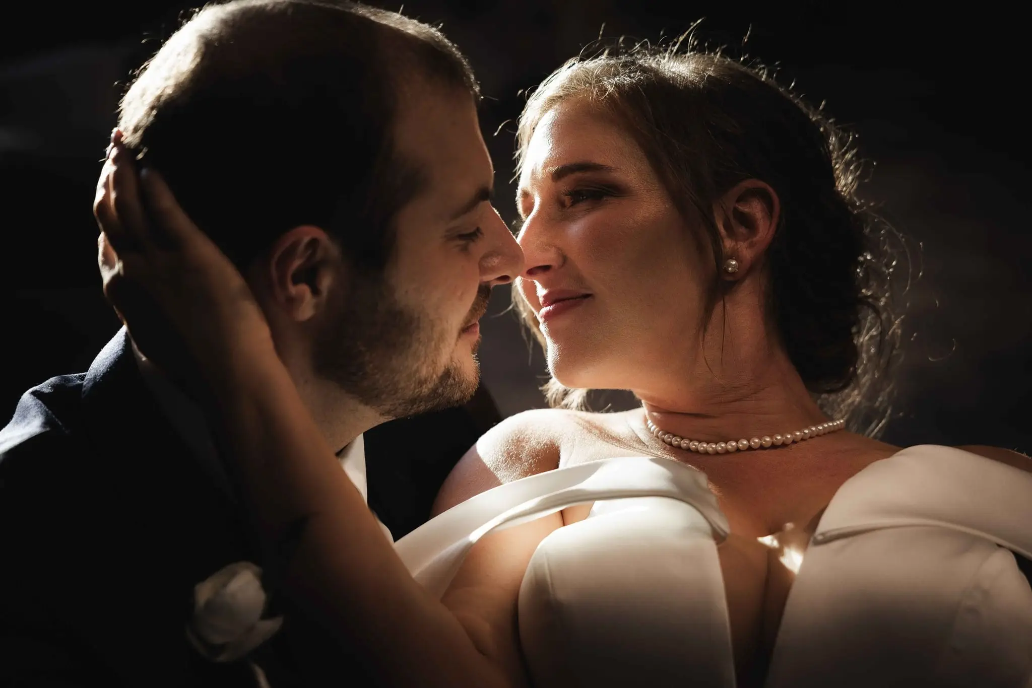 Couple nose to nose in warm side light, the groom's hand in the bride's hair