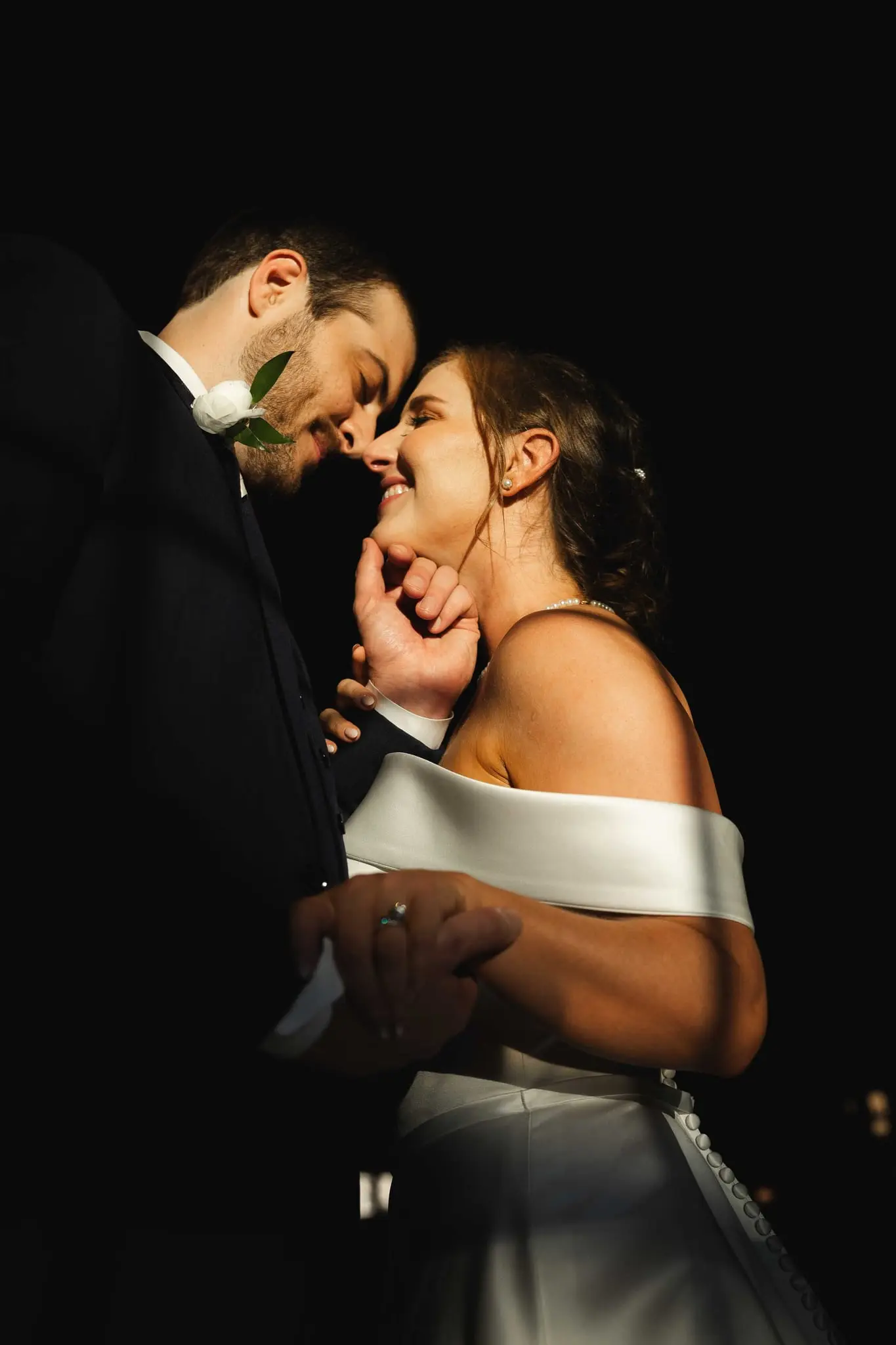 Close portrait of Ashley and Alex nose to nose, his hand cradling her chin in low light