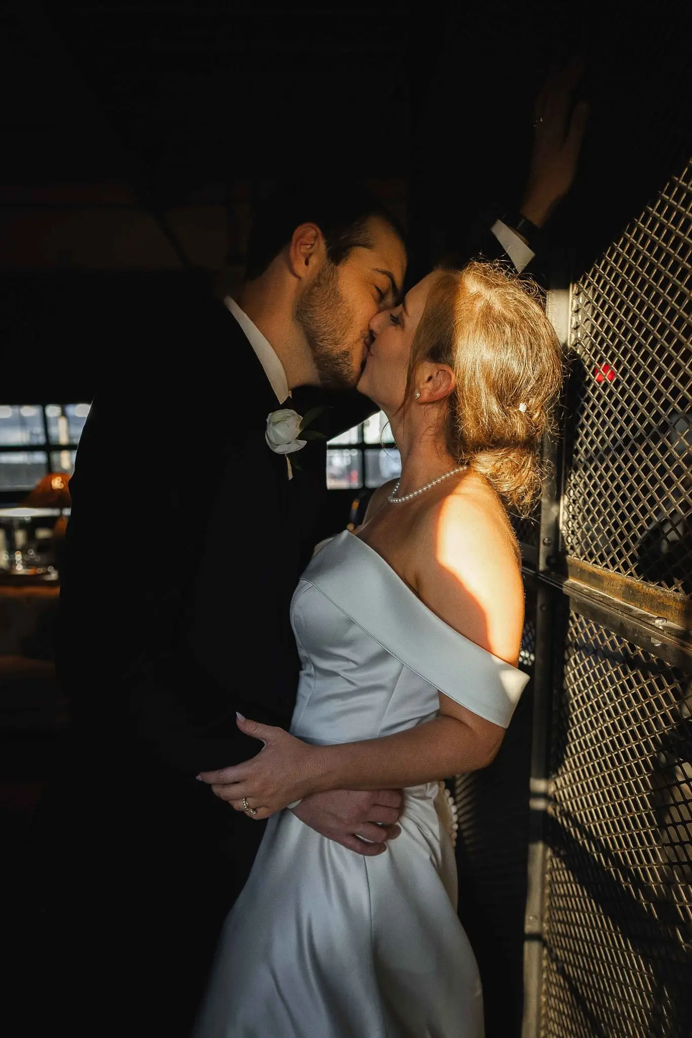 Couple kissing against a metal lattice screen in a bar with warm window light