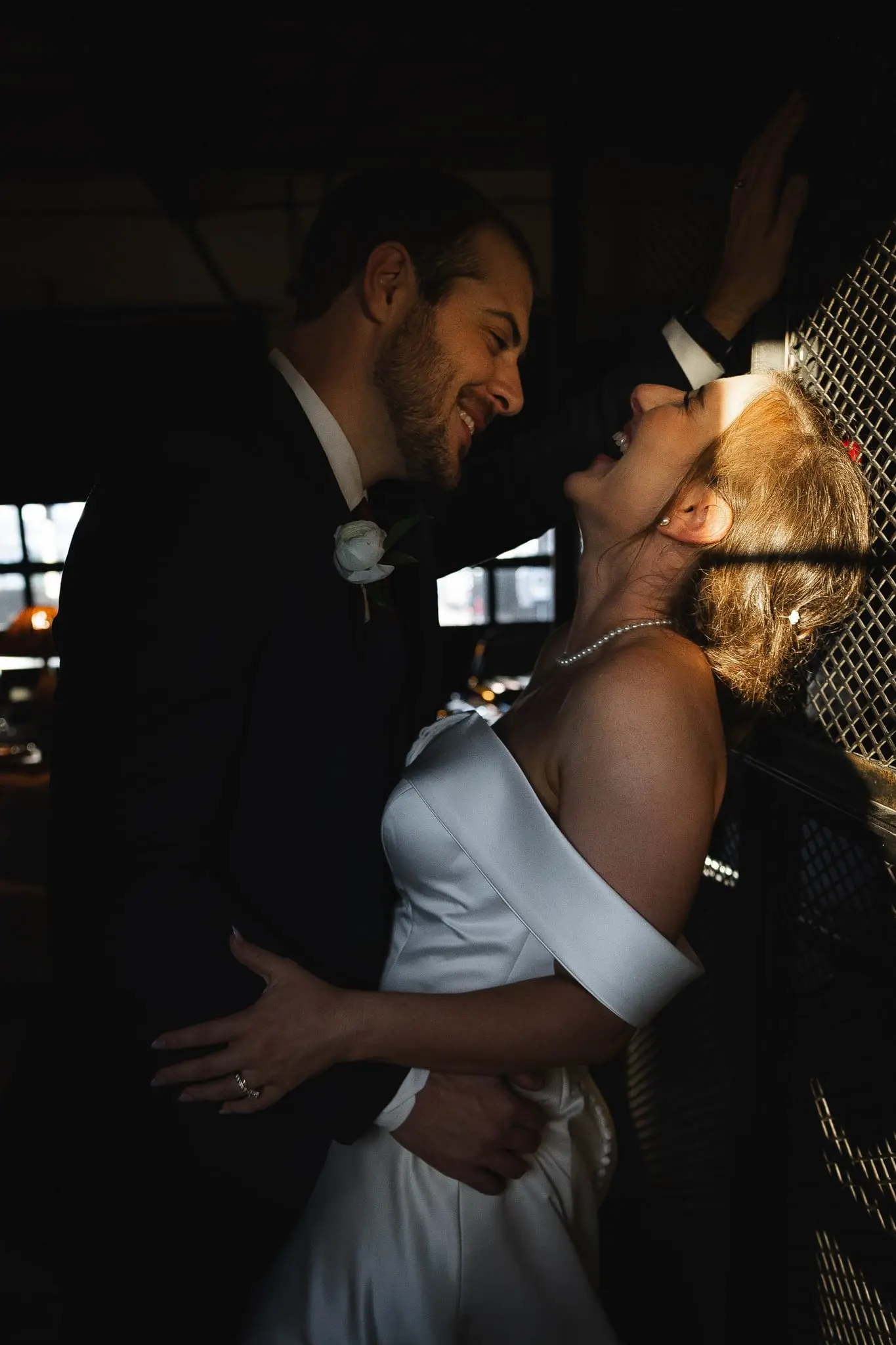 Bride laughing with her head thrown back as the groom leans into her beside the lattice