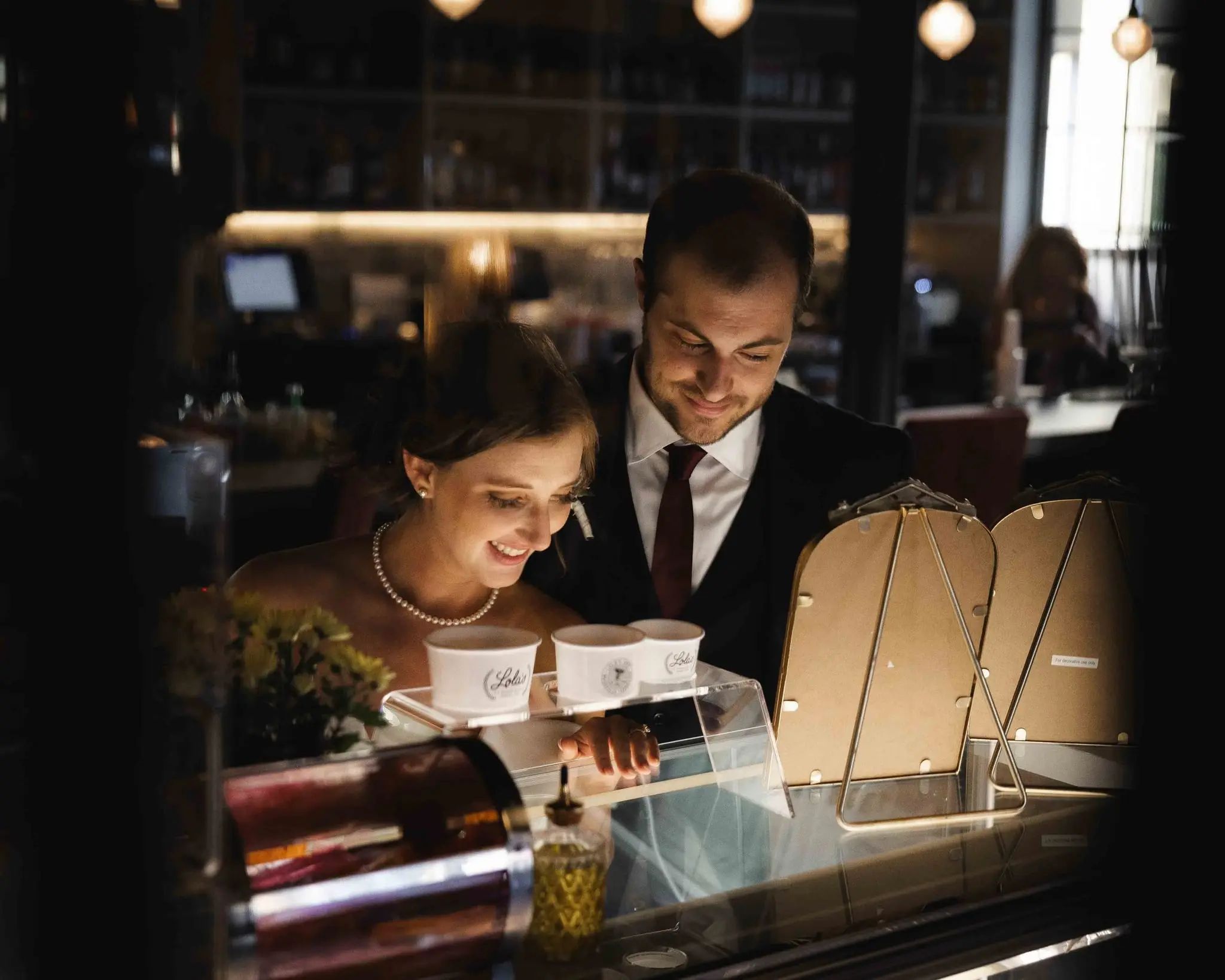 Bride smiling down at ice cream cups on a dessert counter while the groom looks on