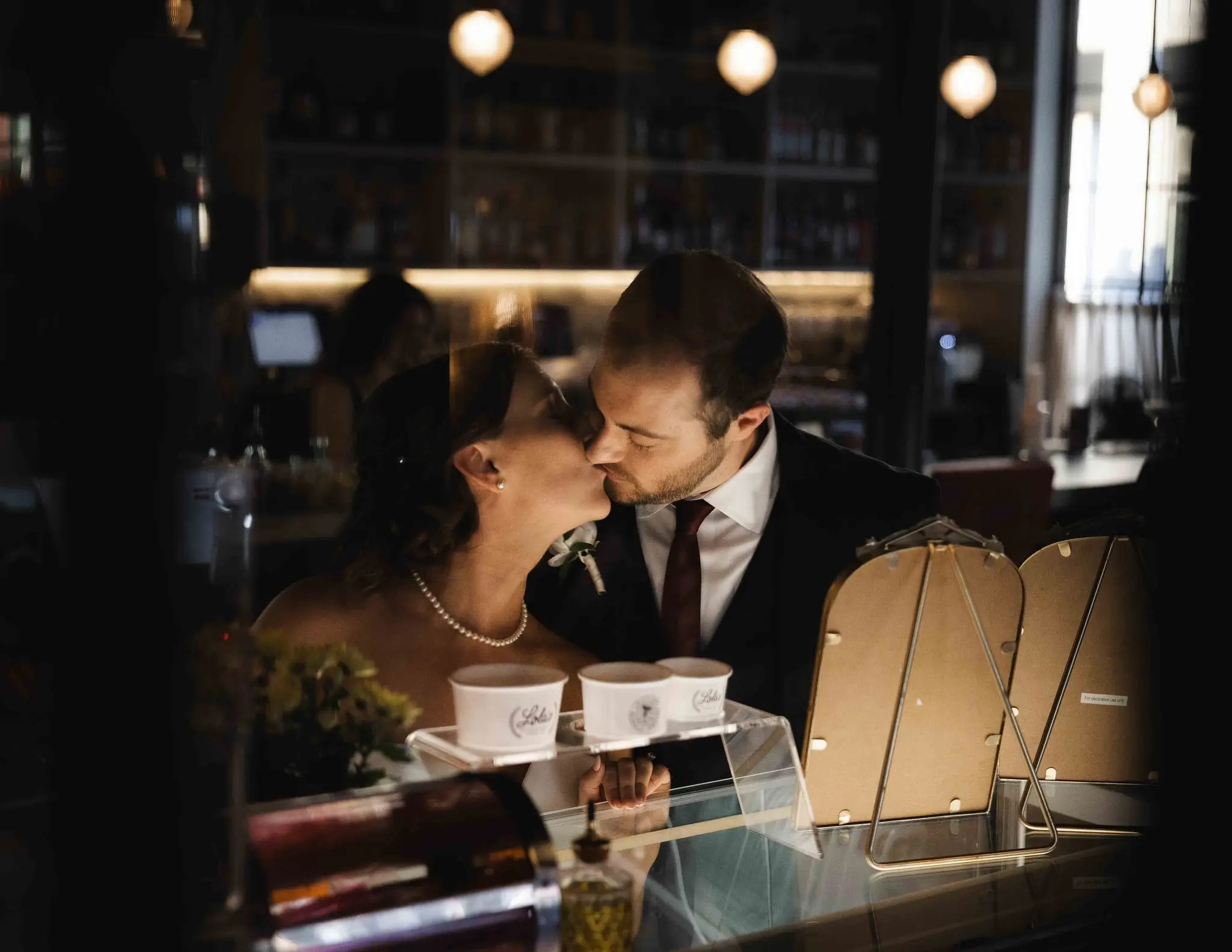 Couple kissing over a dessert counter with glowing pendant lights behind them