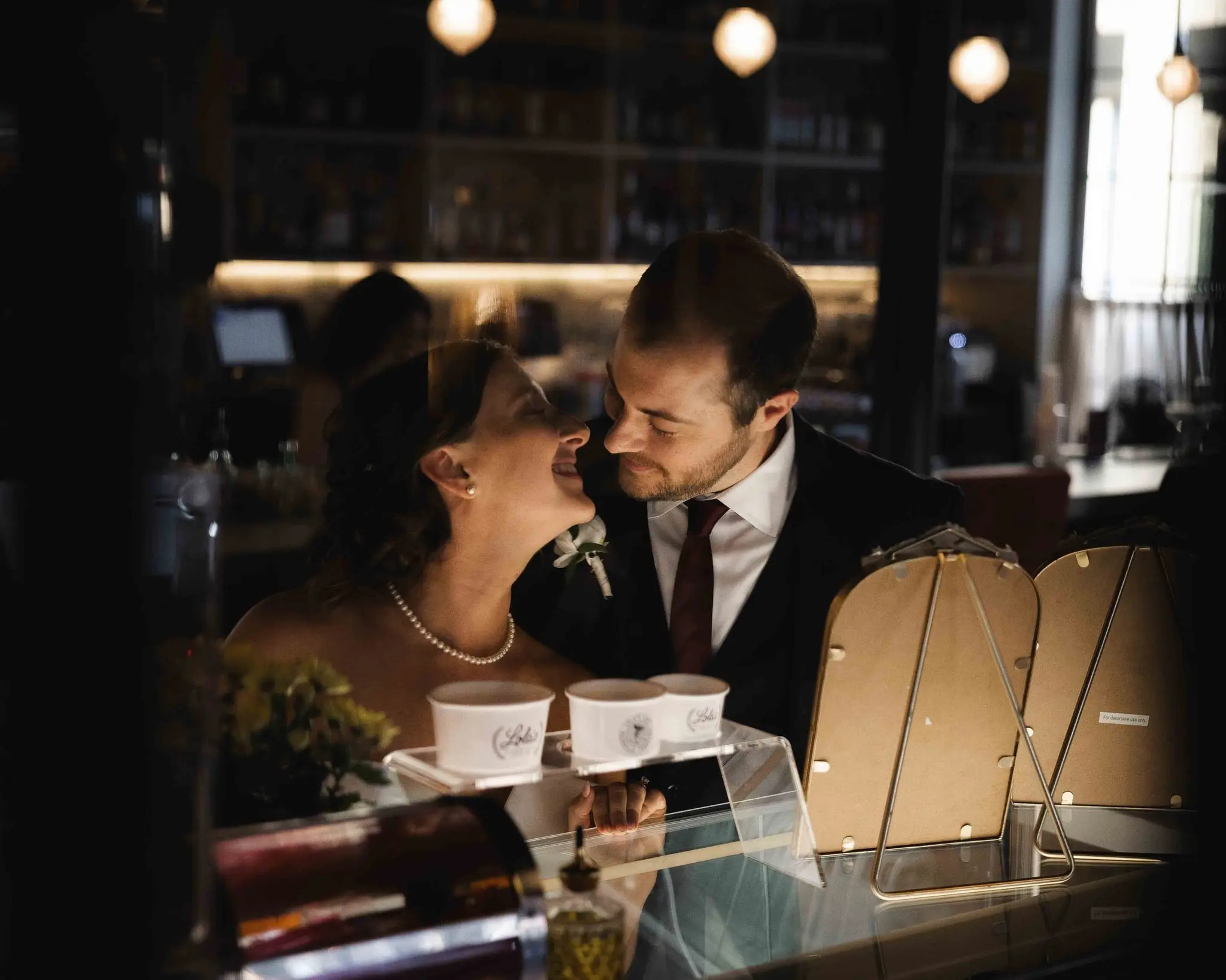 Ashley and Alex grinning together at the dessert counter beneath glass pendant lights