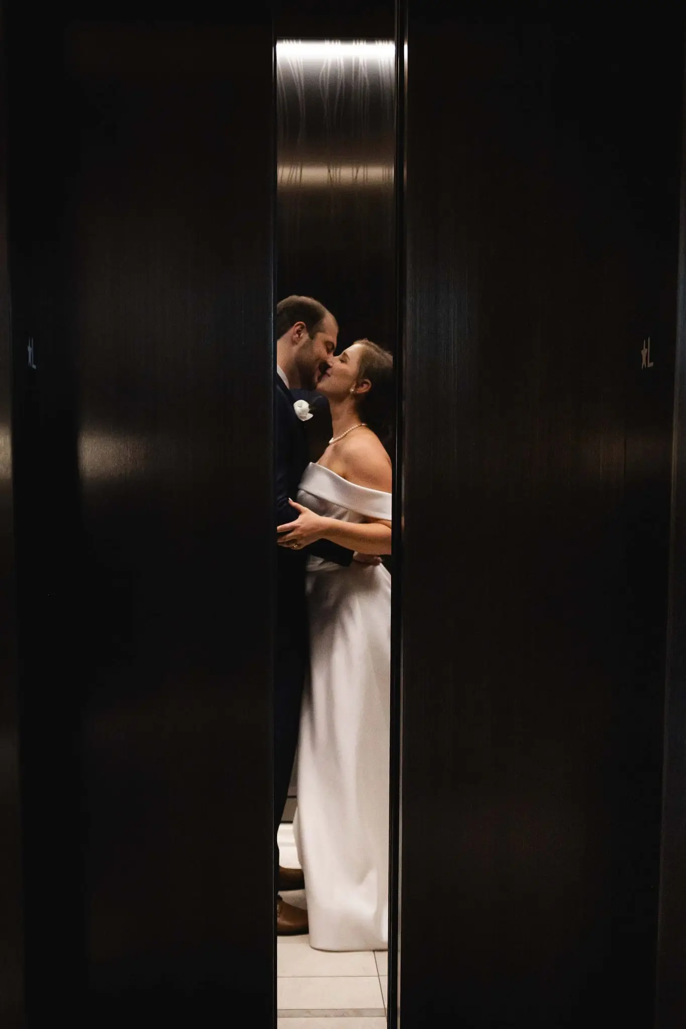 Couple kissing in a narrow gap between two dark elevator doors