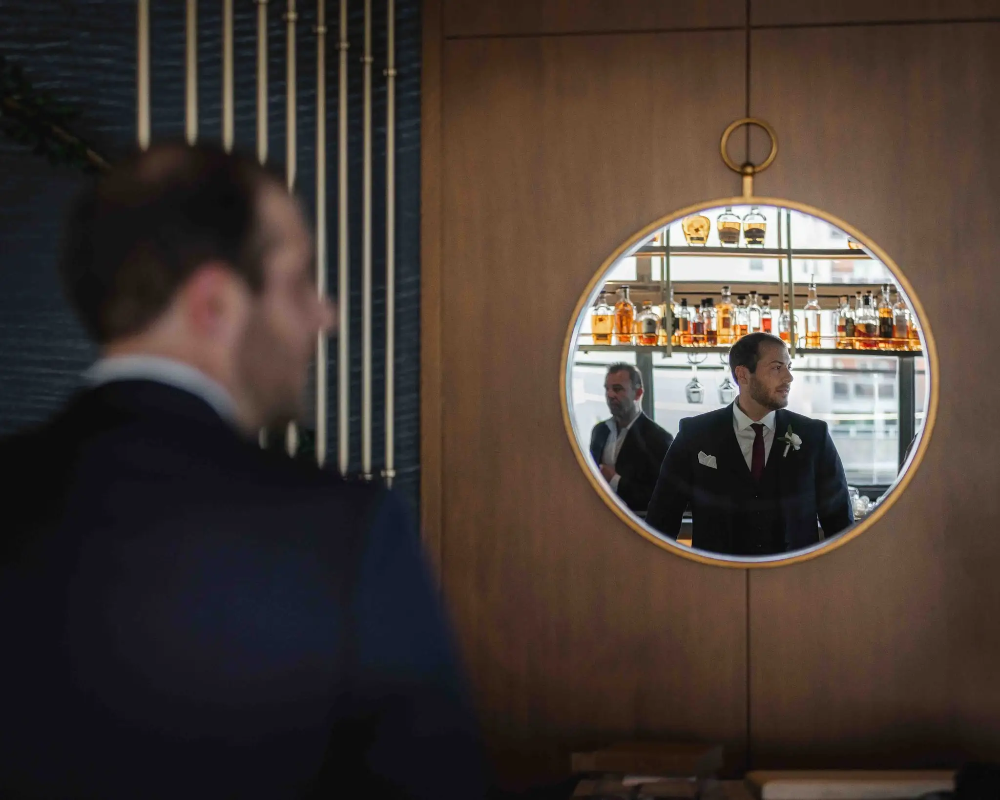 Ashley and Alex wedding at Conrad Nashville, Nashville TN — the groom seen from behind facing a round mirror above a bar