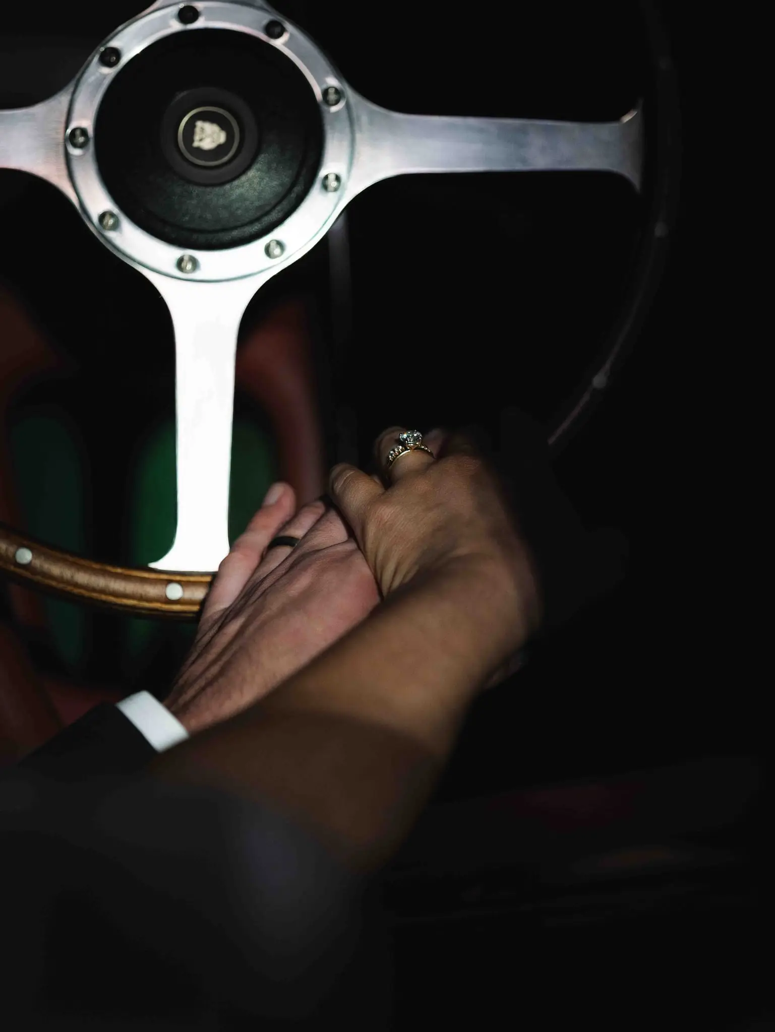 Couple's clasped hands with wedding rings resting on a vintage wooden steering wheel