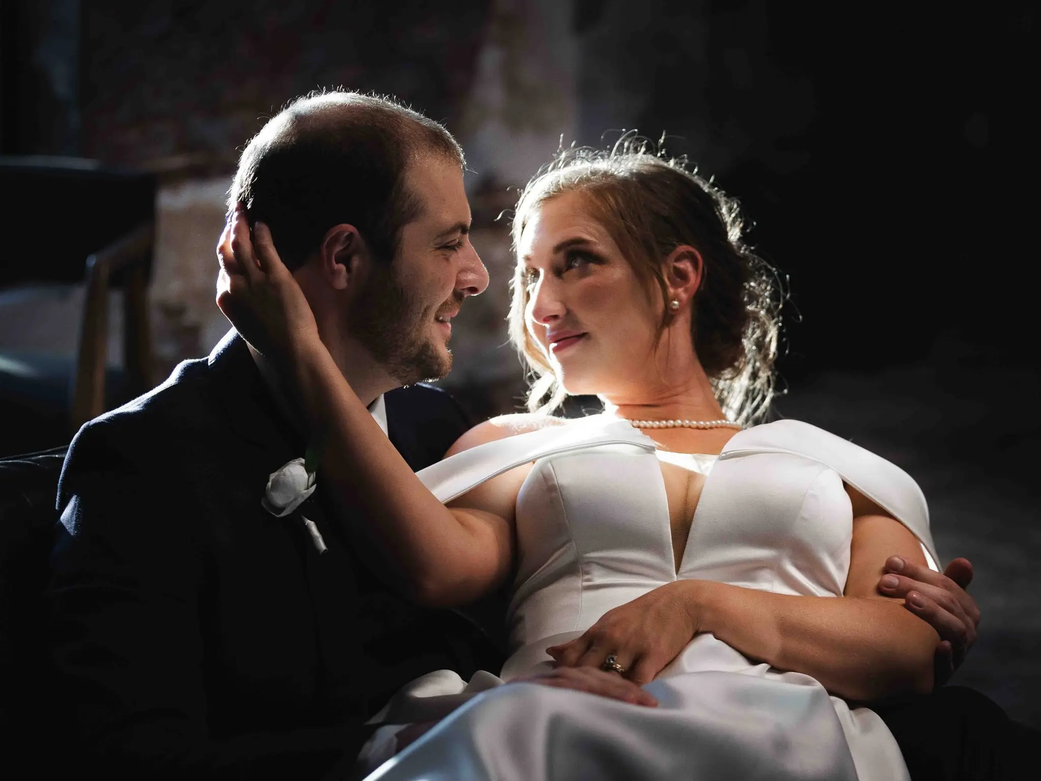 Bride reclining in the groom's lap and looking up at him, his hand at her cheek