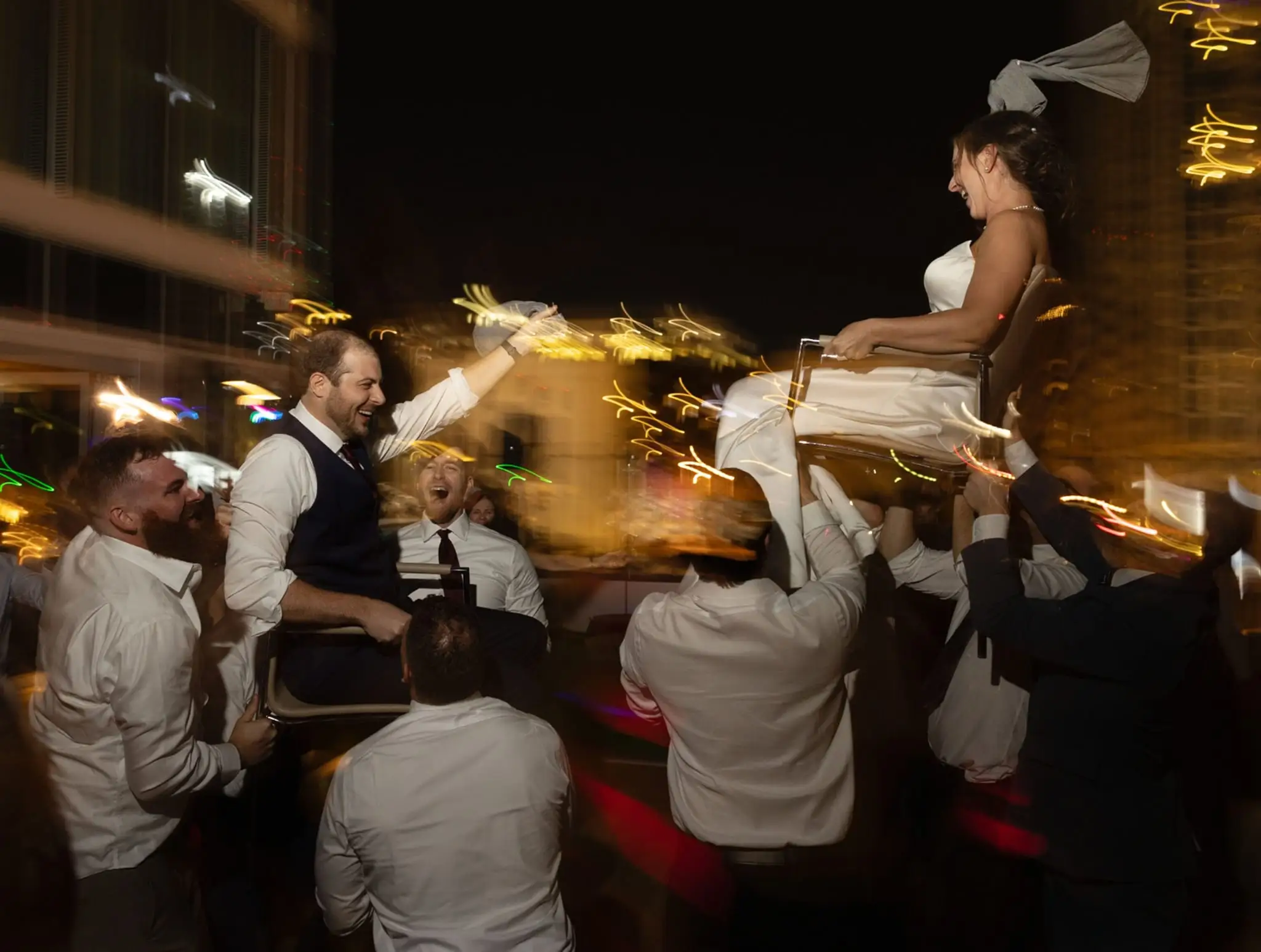 Guests lifting the bride high in a chair on a crowded dance floor