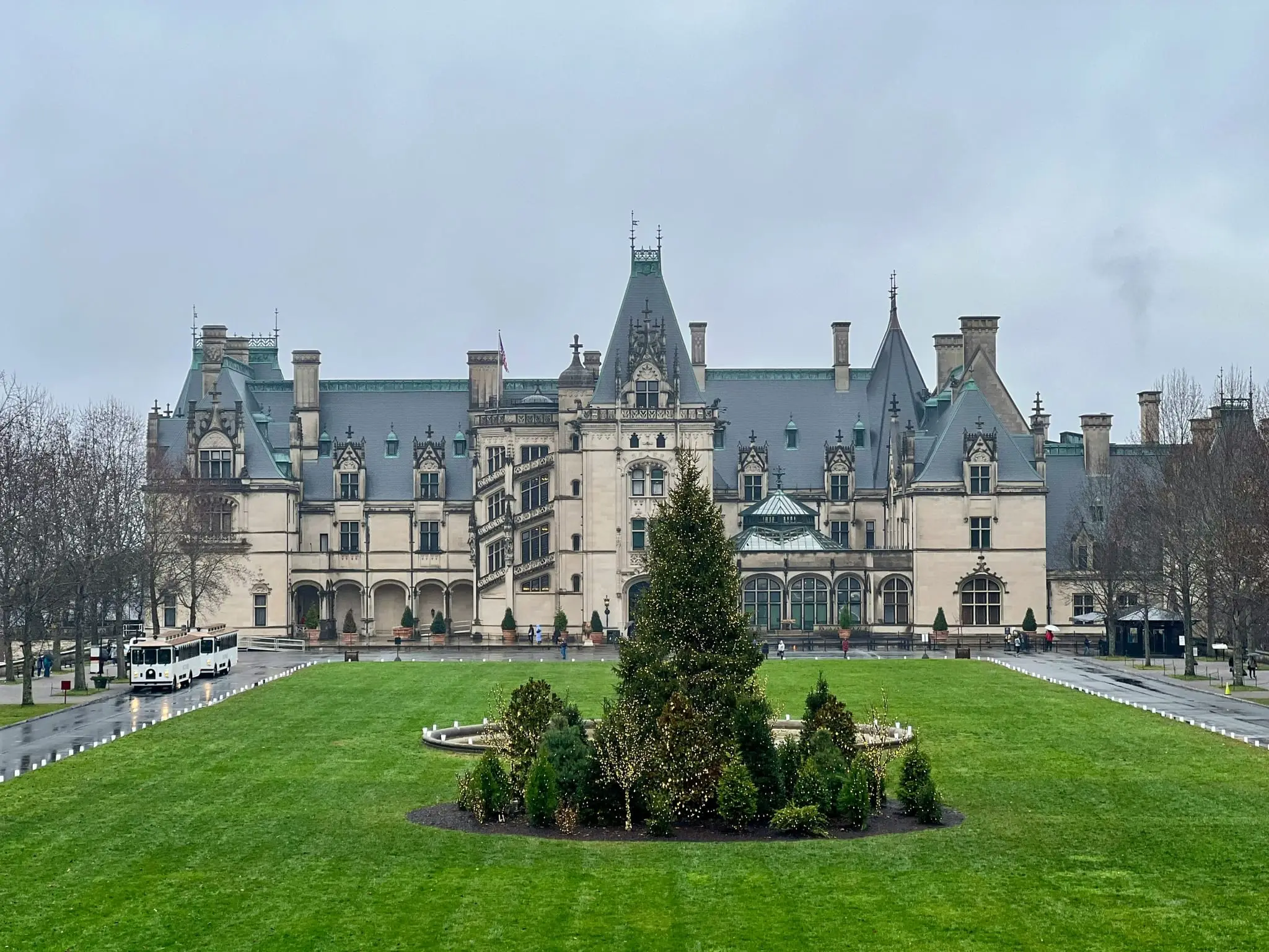 Biltmore House seen across the front lawn, with manicured grounds and a tour trolley in Asheville