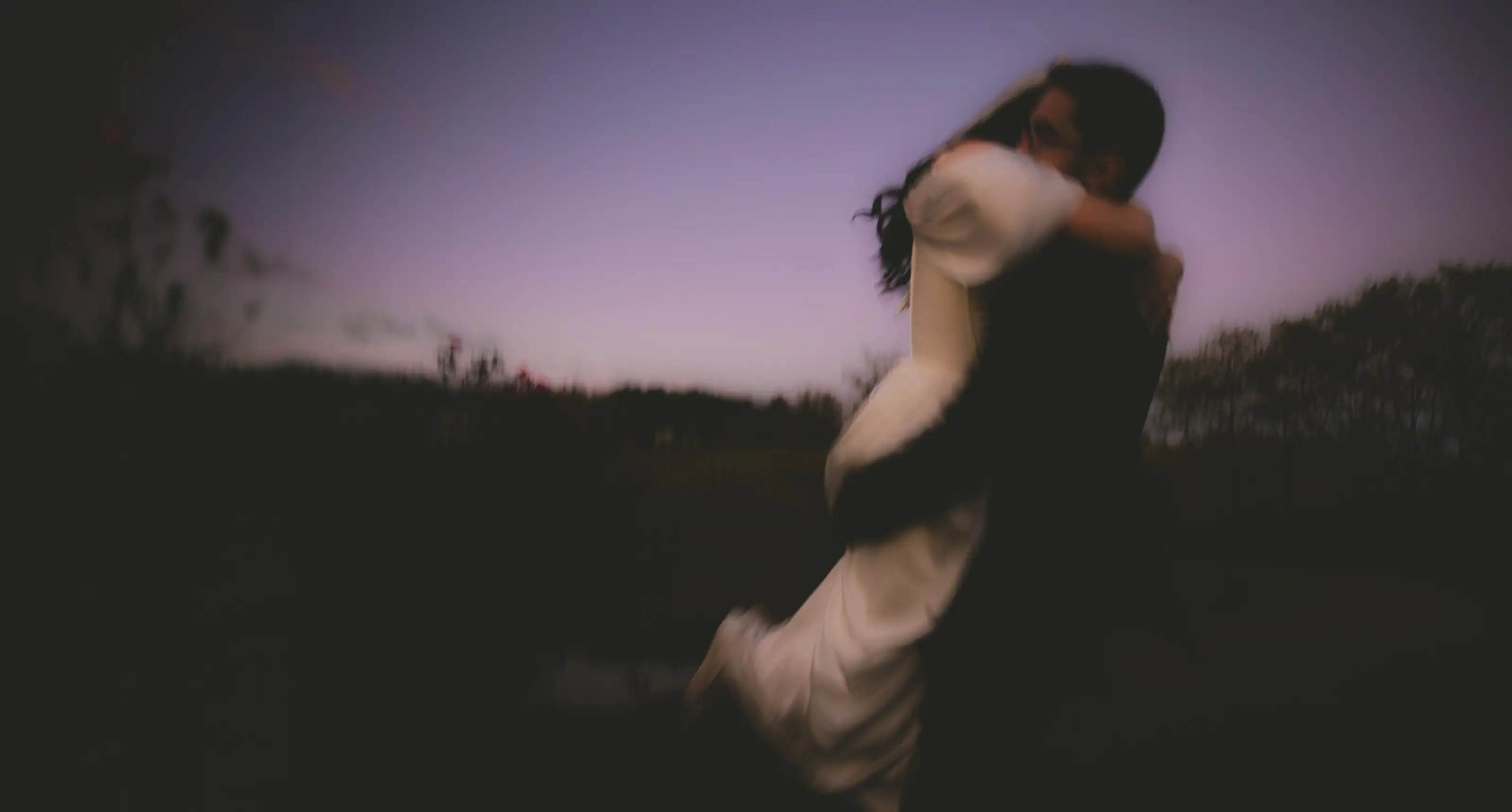 Motion-blurred spin, the groom swinging the bride through the air at dusk